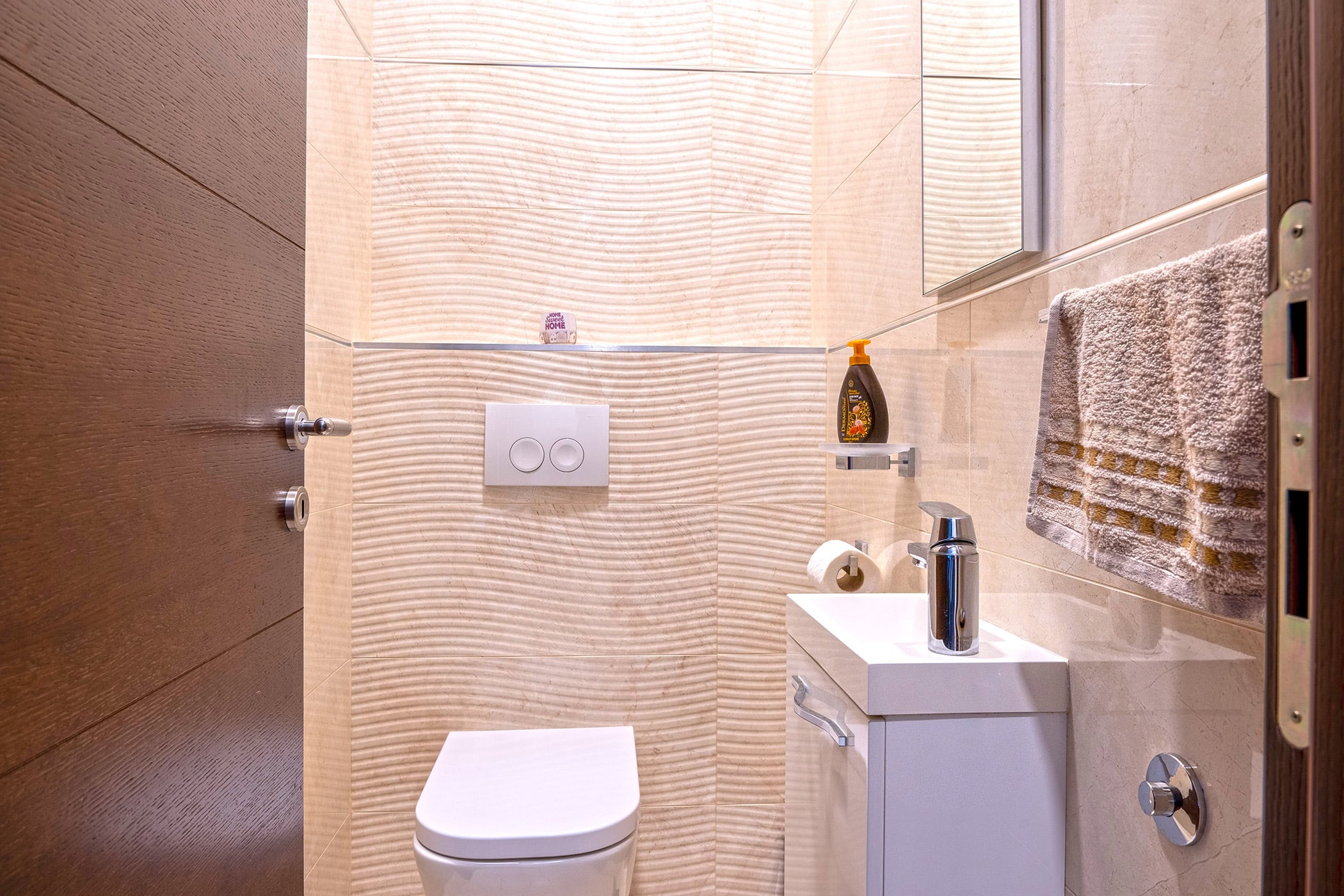 Modernes Badezimmer mit Hänge-WC und Waschbecken in einer Wohnung in Budva, Montenegro, mit beiger Fliesenverkleidung.