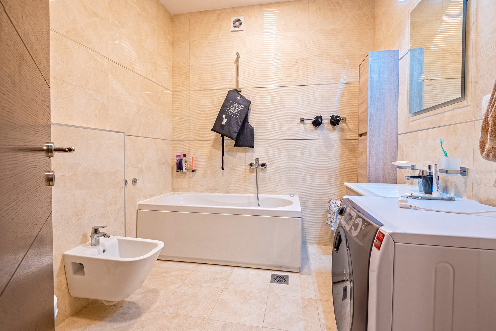 Modernes Badezimmer mit weißer Badewanne, Bidet und Waschmaschine in einer Wohnung in Budva, Montenegro. Beige Fliesen.
