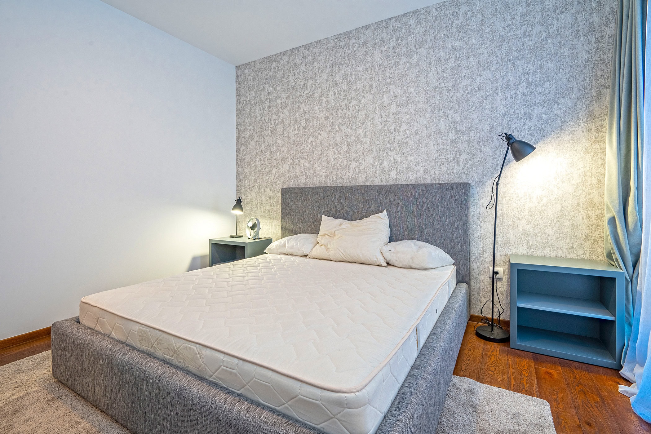Modernes Schlafzimmer in einer Wohnung in Budva, Montenegro: Doppelbett, graue Nachttische, Stehlampe und Akzentwand.