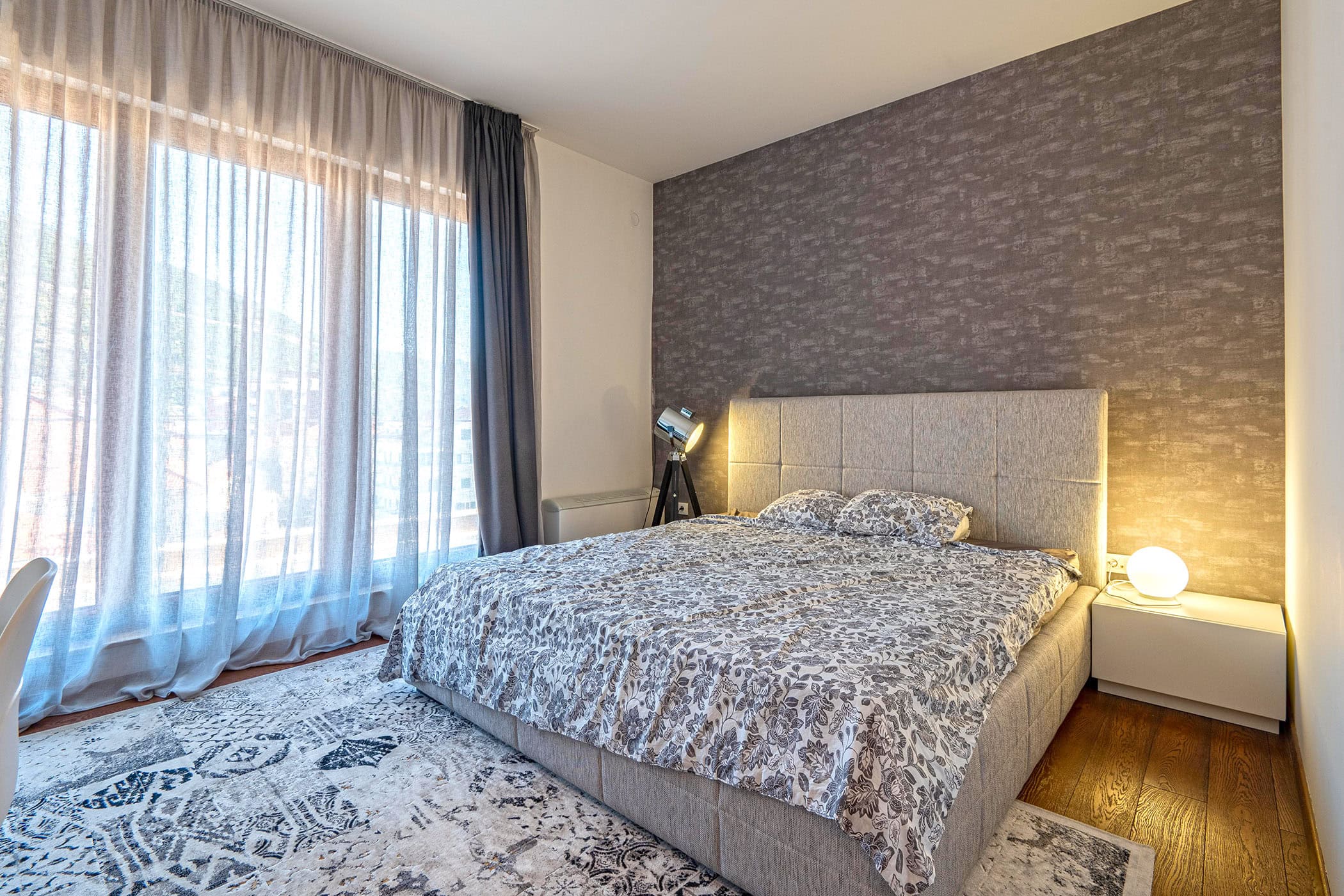 Modernes Schlafzimmer mit Doppelbett in einer Wohnung in Budva, Montenegro: Panoramafenster, stilvolle Dekoration und Beleuchtung.