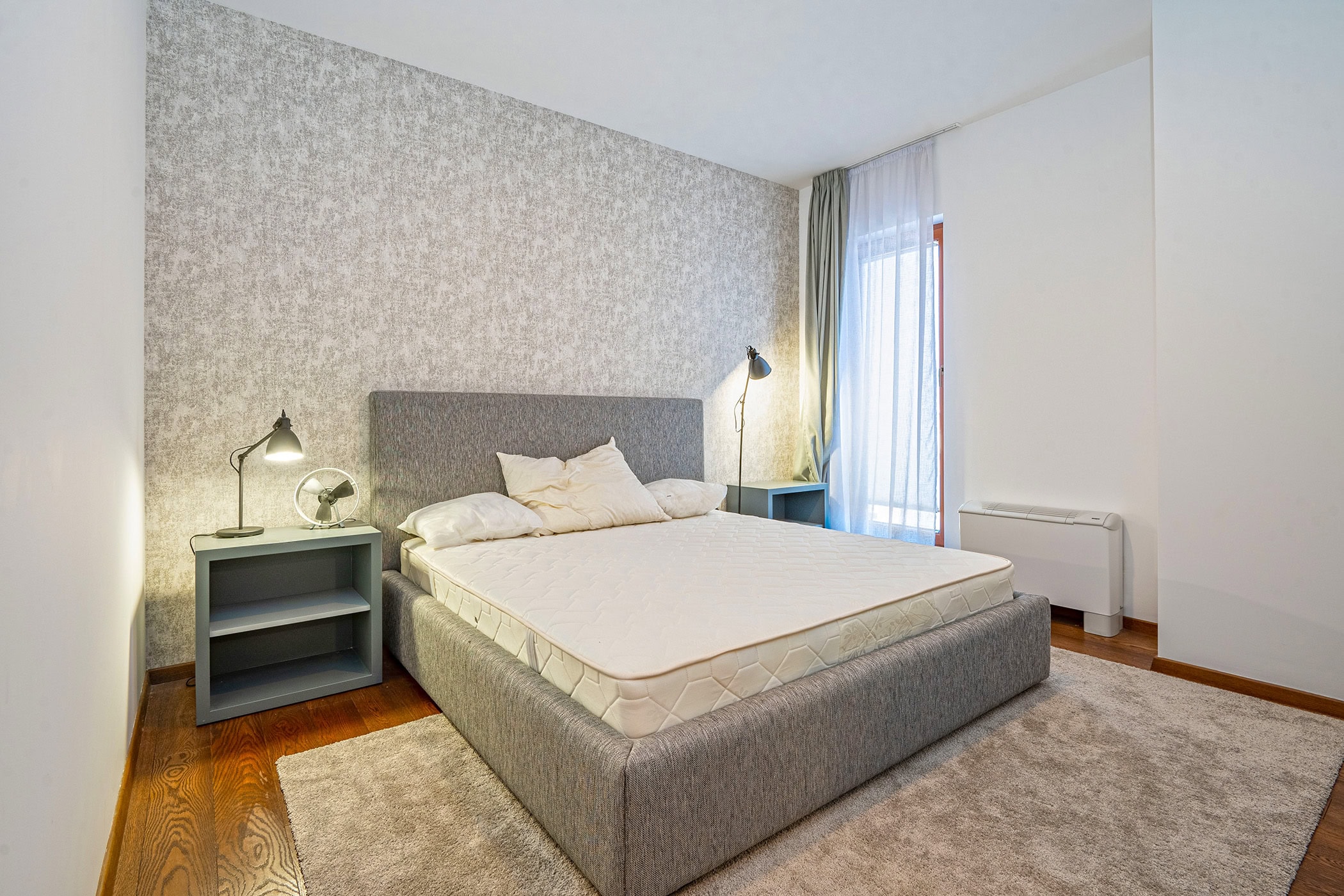 Gemütliches Schlafzimmer mit Doppelbett in einer Wohnung in Budva, Montenegro: graue Tapete, Parkett und Zugang zum Balkon.