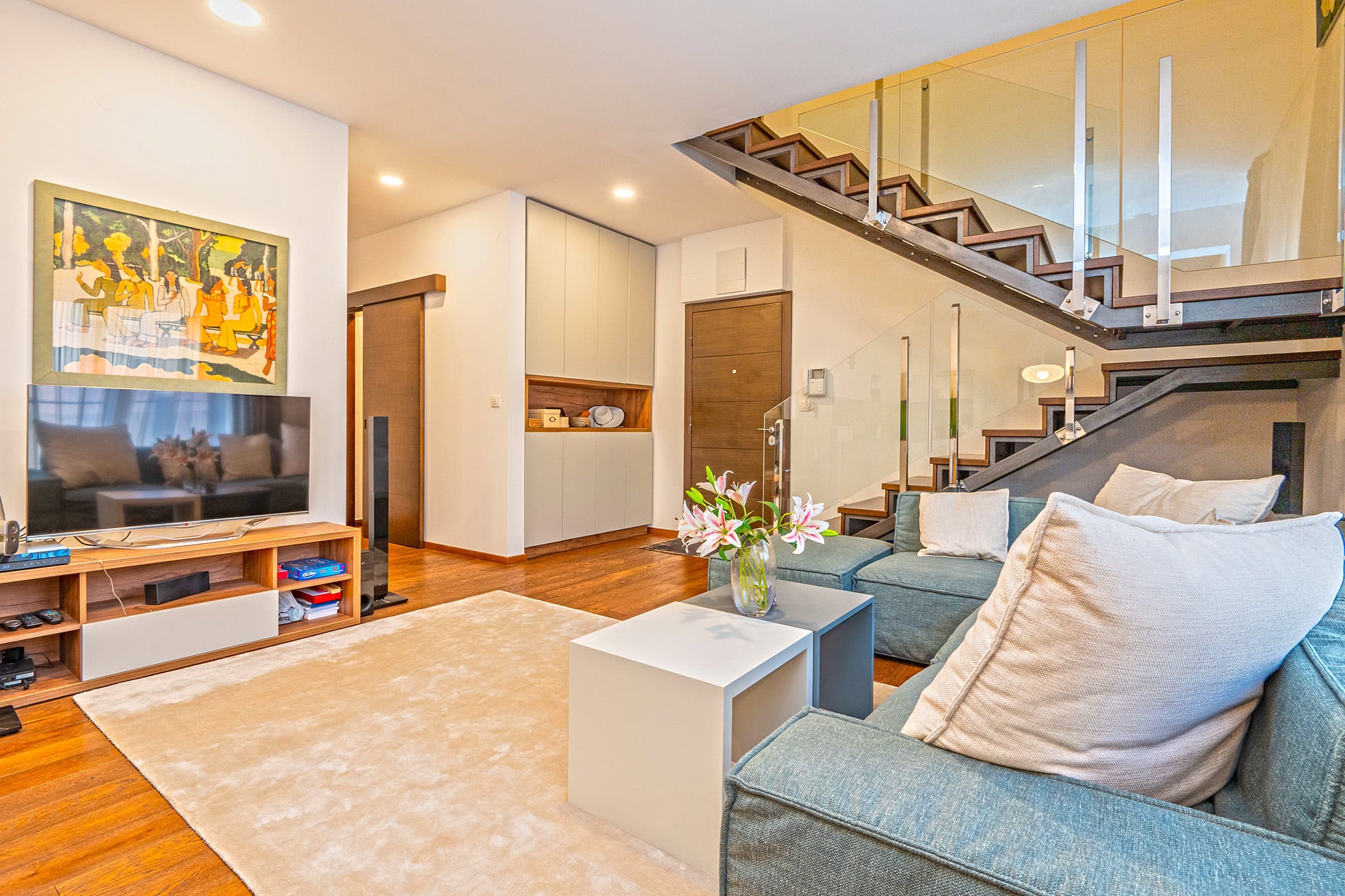 Wohnzimmer in einem Duplex in Budva, Montenegro: moderne Möbel, helles Sofa und stilvolle Treppe mit Glas.