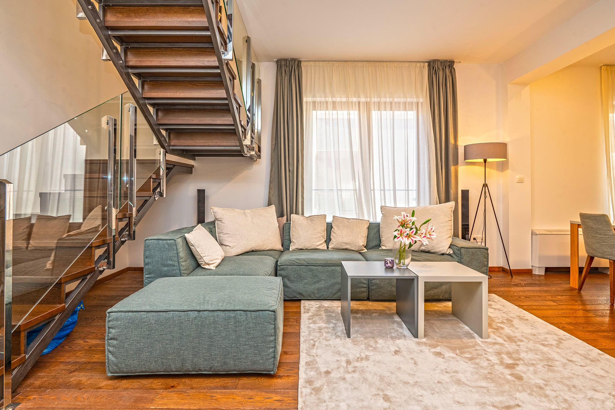 Wohnzimmer in einem Duplex in Budva, Montenegro: modernes Sofa, Holztreppe mit Glas und Parkettboden.