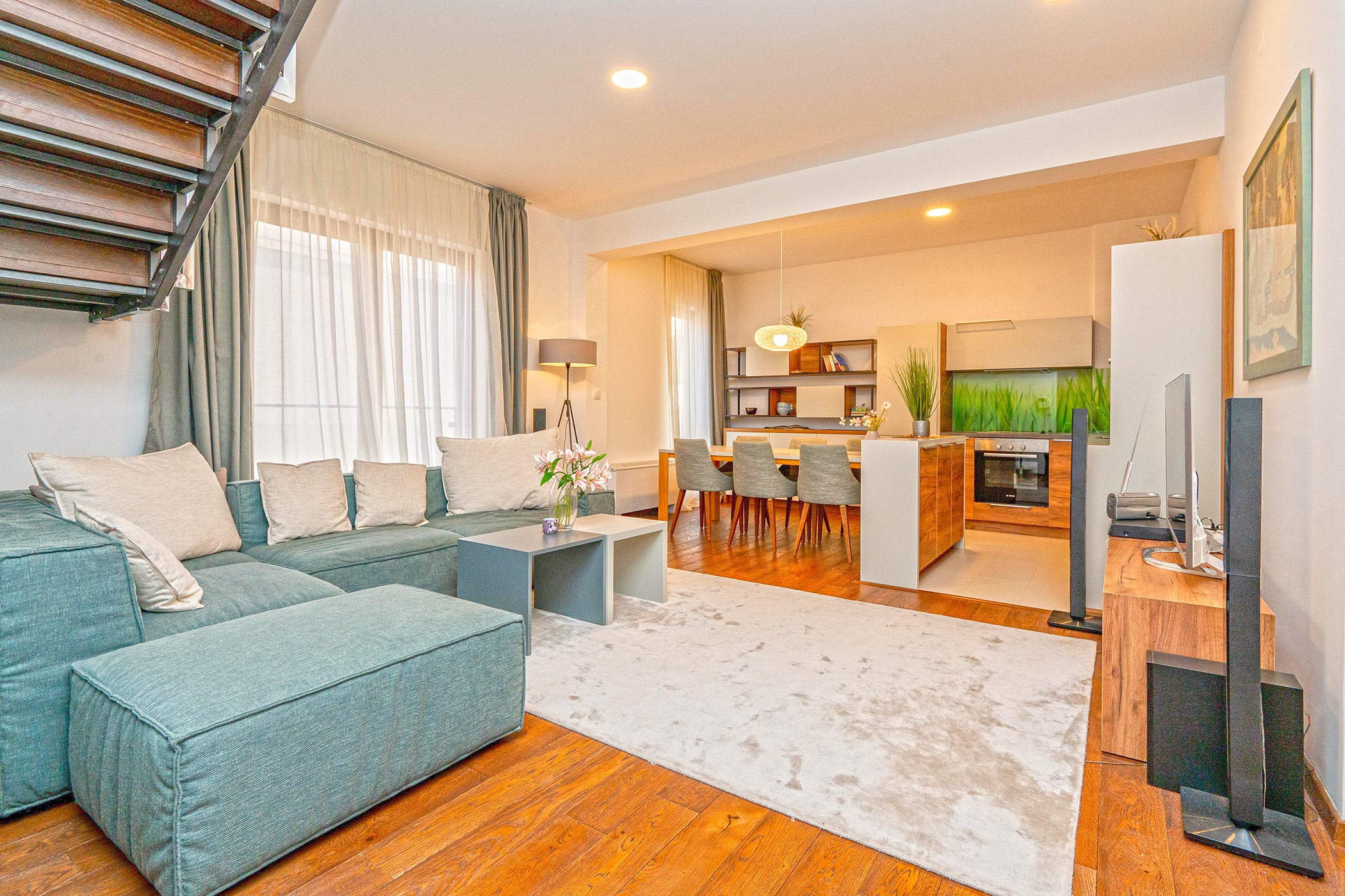 Wohnzimmer in einem Duplex in Budva, Montenegro: moderne Küche, Essbereich, weiches Sofa und Treppe ins zweite Stockwerk.
