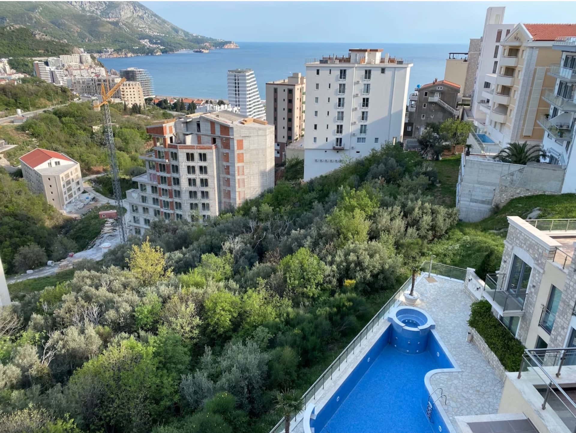 Blick von der Terrasse auf den Pool, das Meer und die Berge in Bečići, Montenegro: Panorama des Ferienorts und der Wohnanlage mit viel Grün.