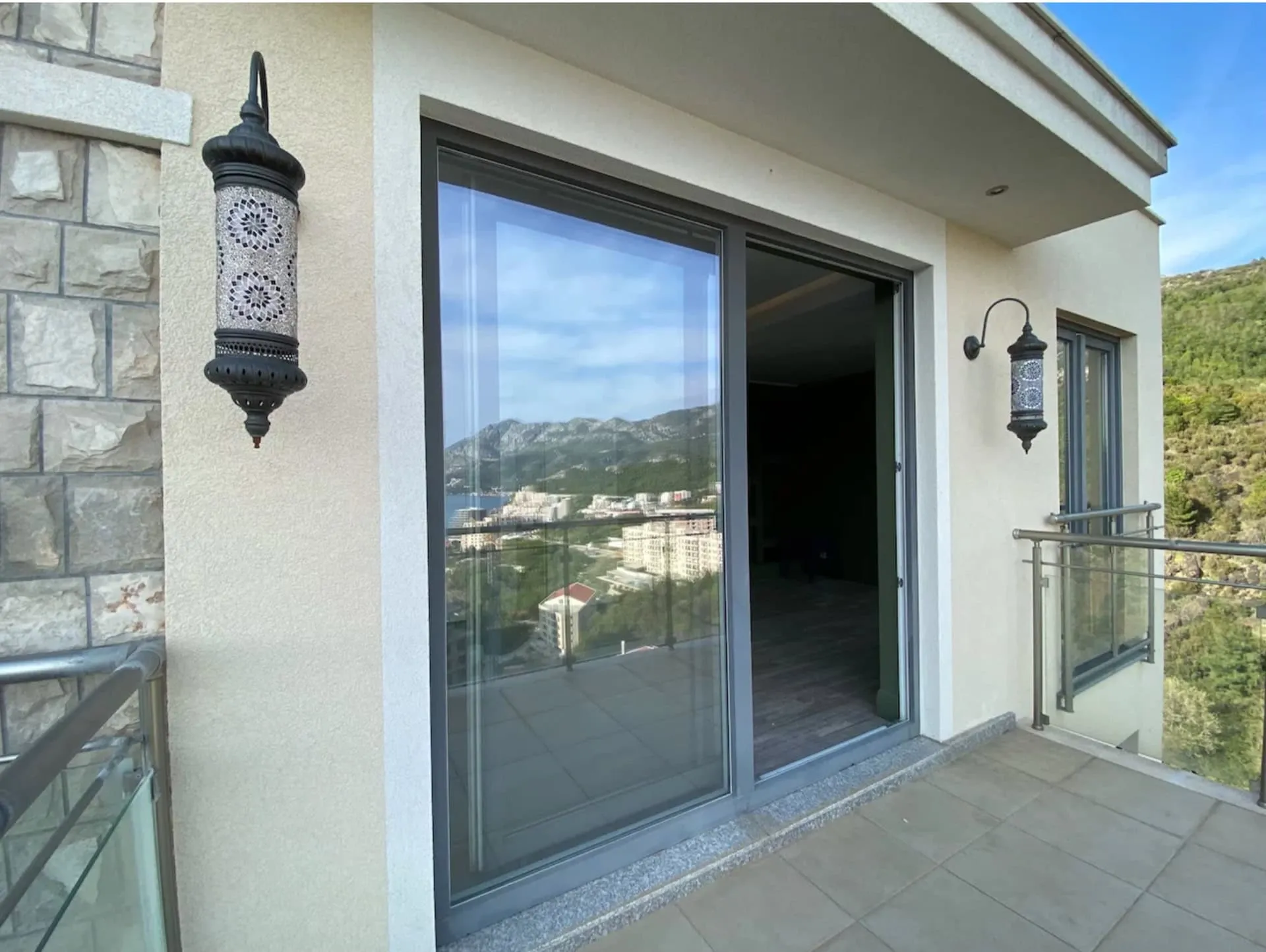 Balcony with panoramic mountain and sea views in an apartment, Becici, Montenegro: stylish wall lights and glazing.