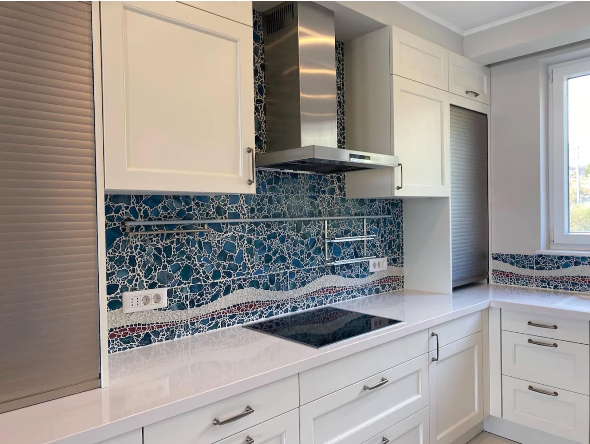Moderne weiße Küche mit Mosaik-Spritzschutz in einer Wohnung in Bečići, Montenegro. Integrierte Geräte und helles Interieur.