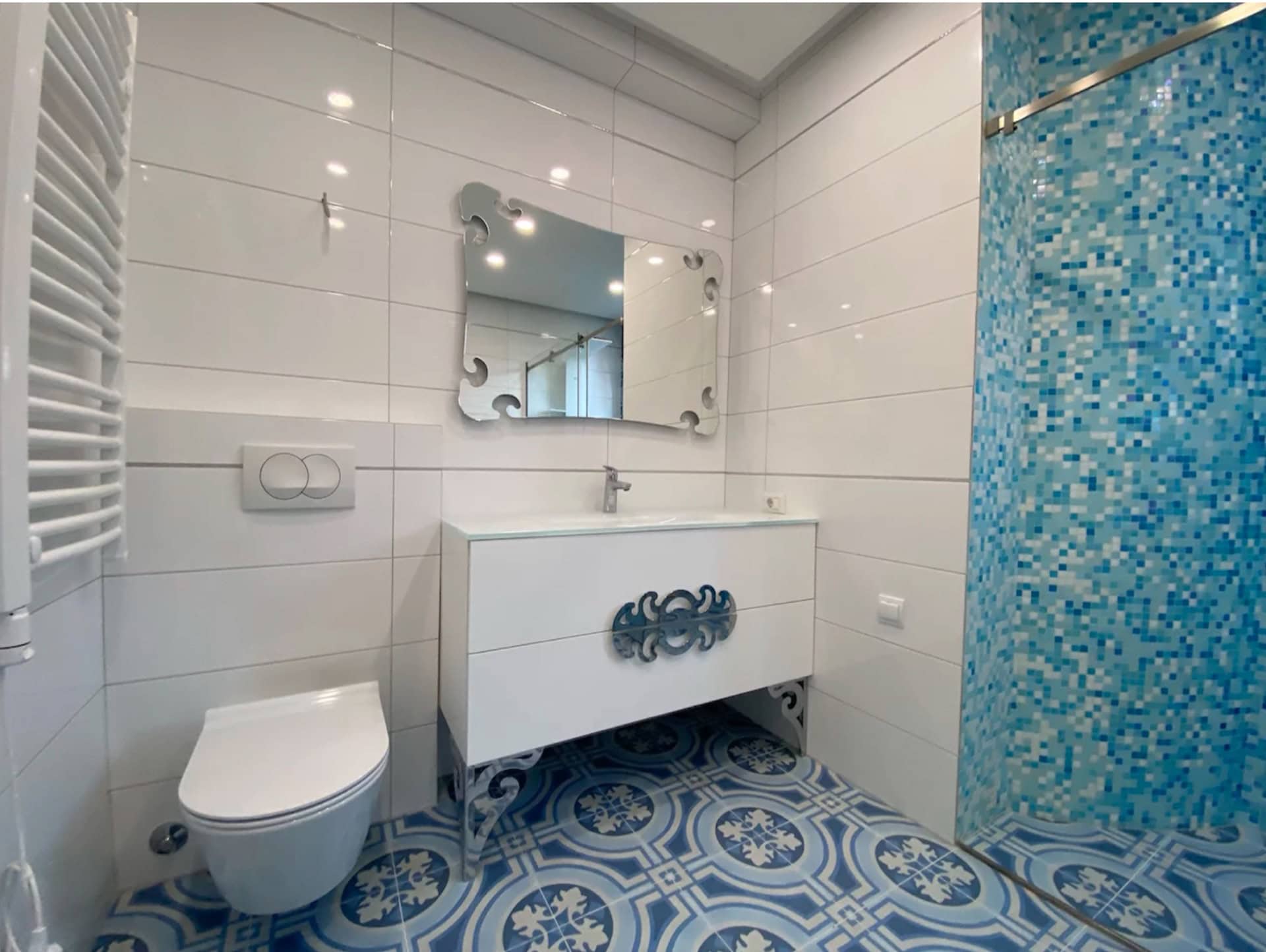 Modernes Badezimmer in einer Wohnung in Bečići, Montenegro: weiße Fliesen, Dusche mit blauer Mosaikverkleidung und gemusterter Boden.