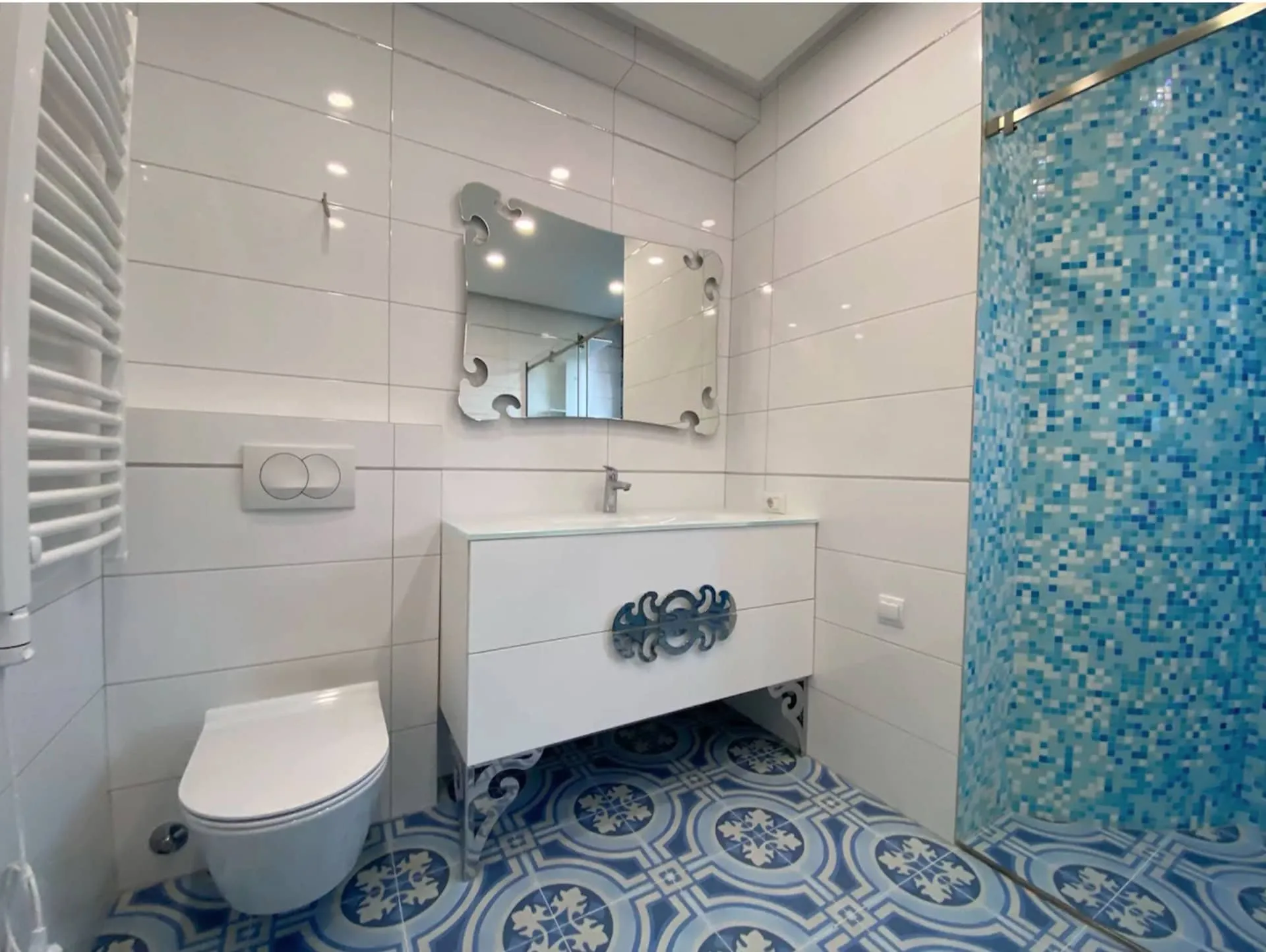 Modern bathroom in an apartment in Bečići, Montenegro: white tiles, a shower with blue mosaic, and patterned flooring.