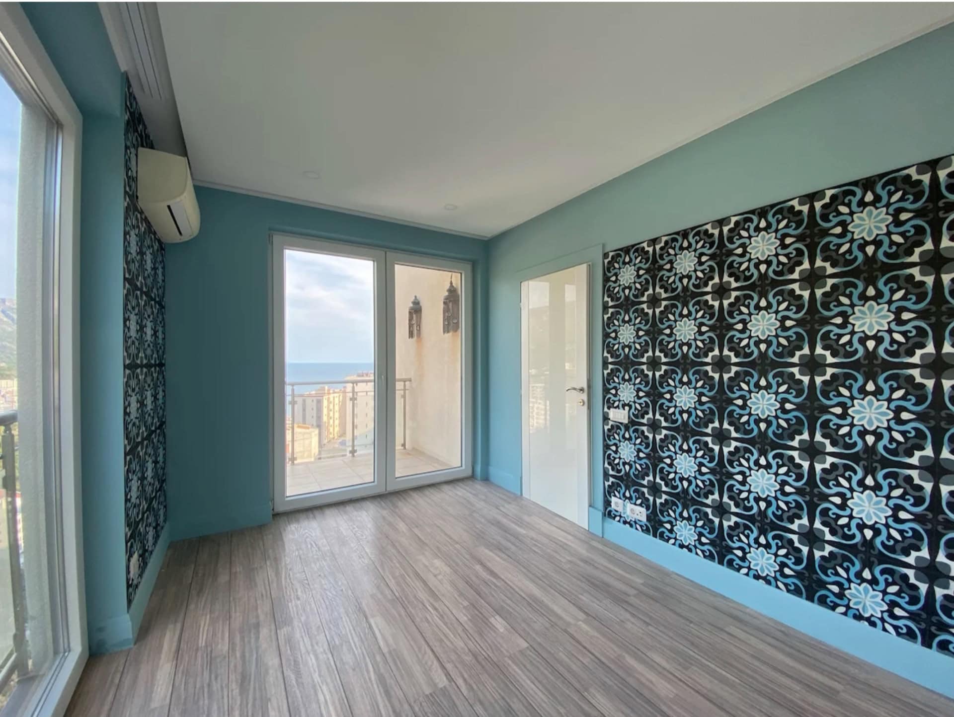 Helles Wohnzimmer in einer Wohnung in Bečići, Montenegro: Panoramafenster, Meerblick, stilvolle Tapeten und Laminatboden.