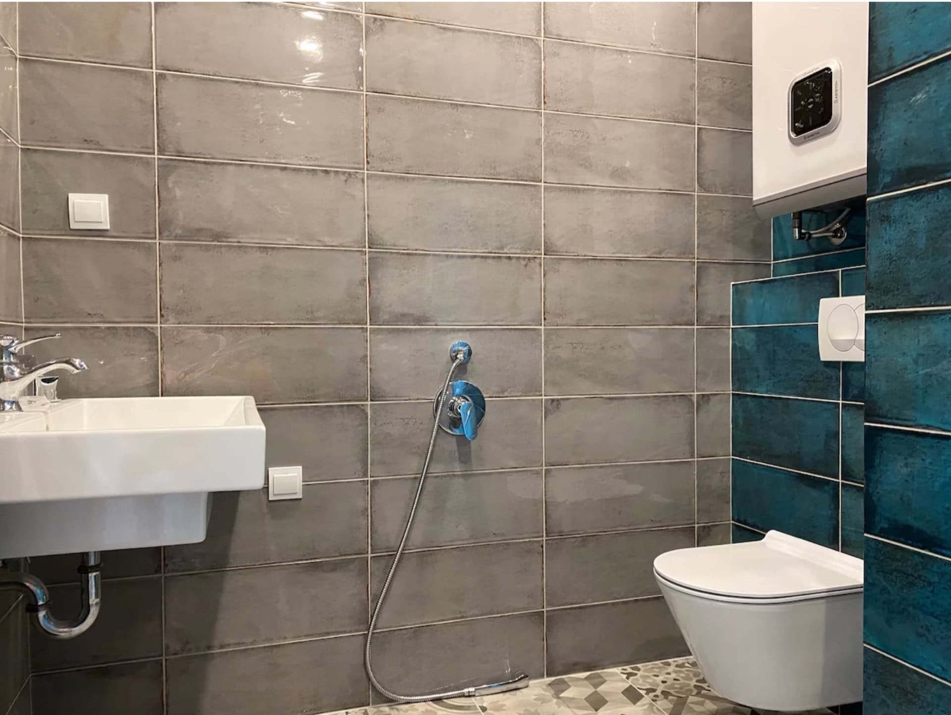 Modernes Badezimmer in einer Wohnung, Bečići, Montenegro: graue Fliesen, wandhängendes WC, Hygienedusche und Boiler.