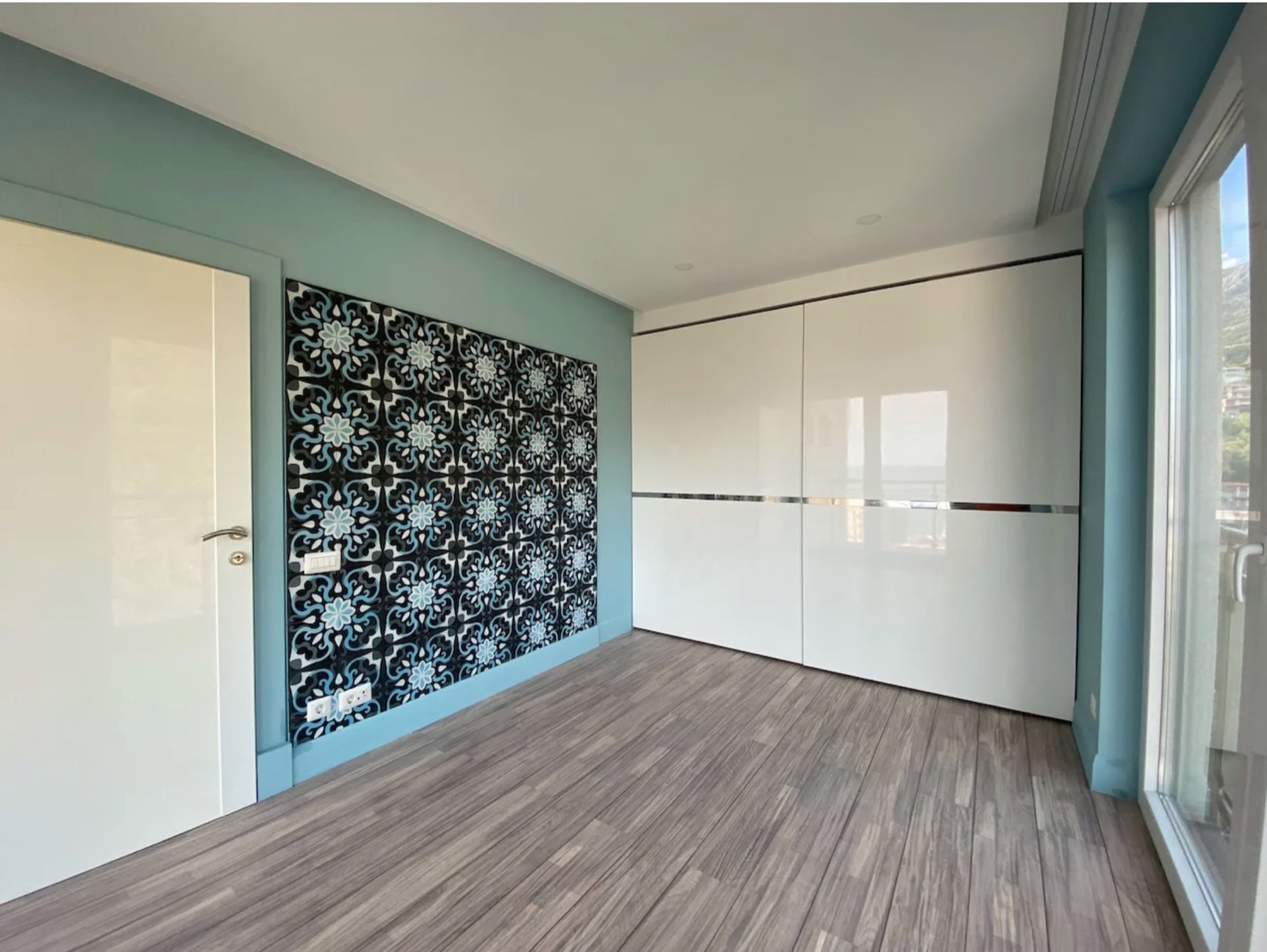 Helles Schlafzimmer mit weißem Schiebetürenschrank und Akzentwand in einer Wohnung in Bečići, Montenegro. Modernes Interieur.