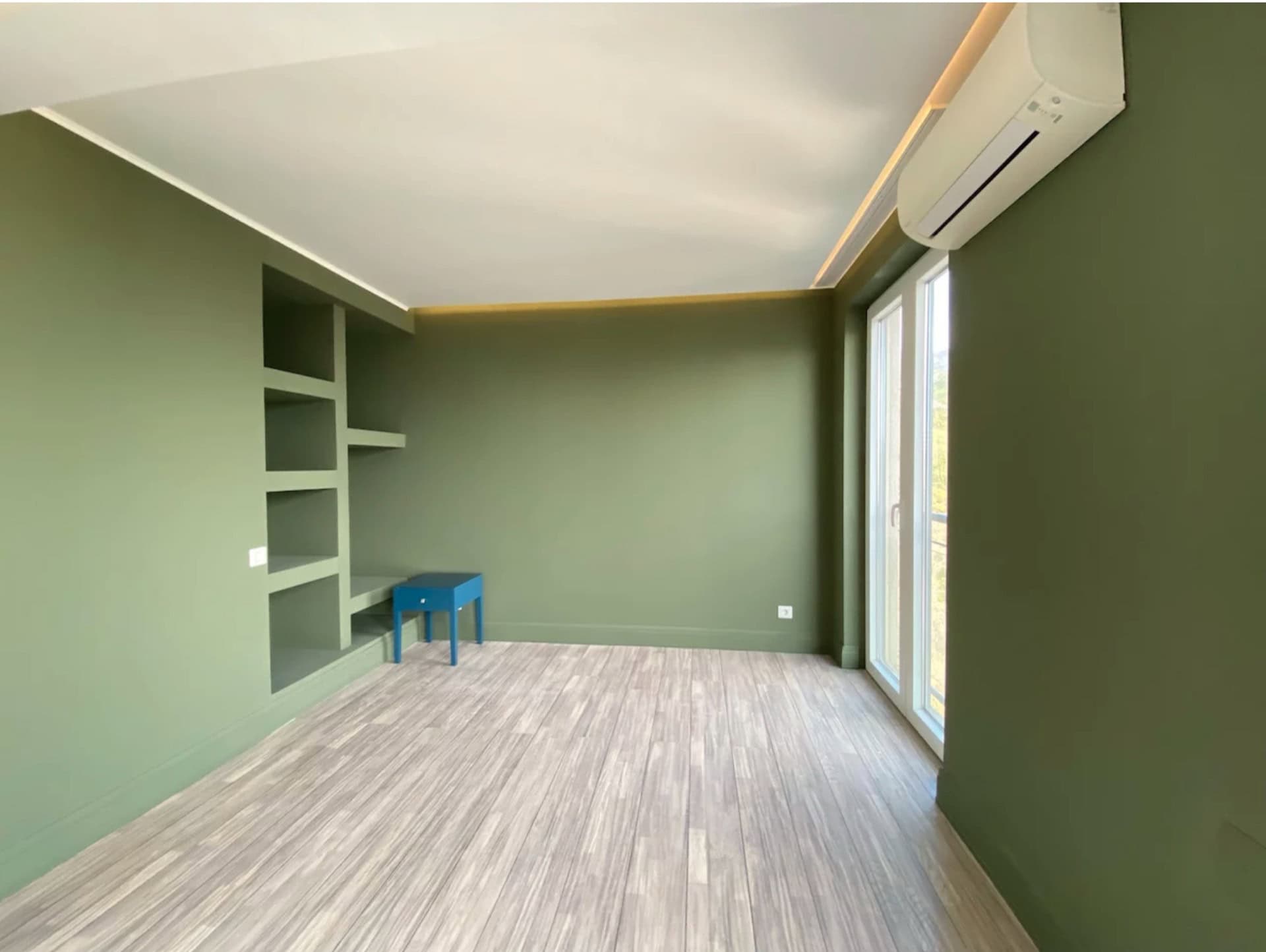 Schlafzimmer in einer Wohnung in Bečići, Montenegro: olivgrüne Wände, eingebaute Regale, heller Boden und Zugang zum Balkon.