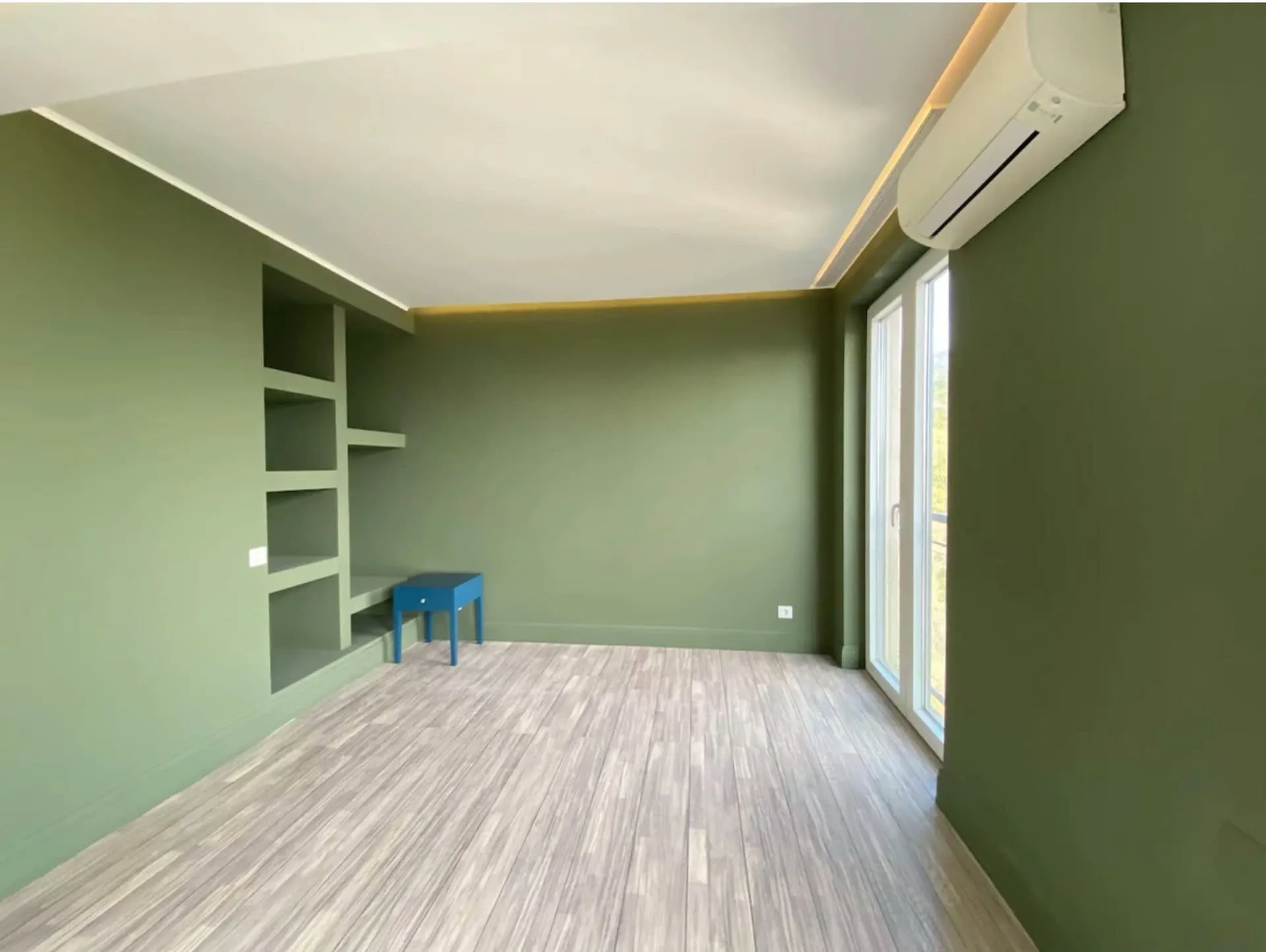 Bedroom in an apartment in Bečići, Montenegro: olive walls, built-in shelves, light flooring, and access to the balcony.
