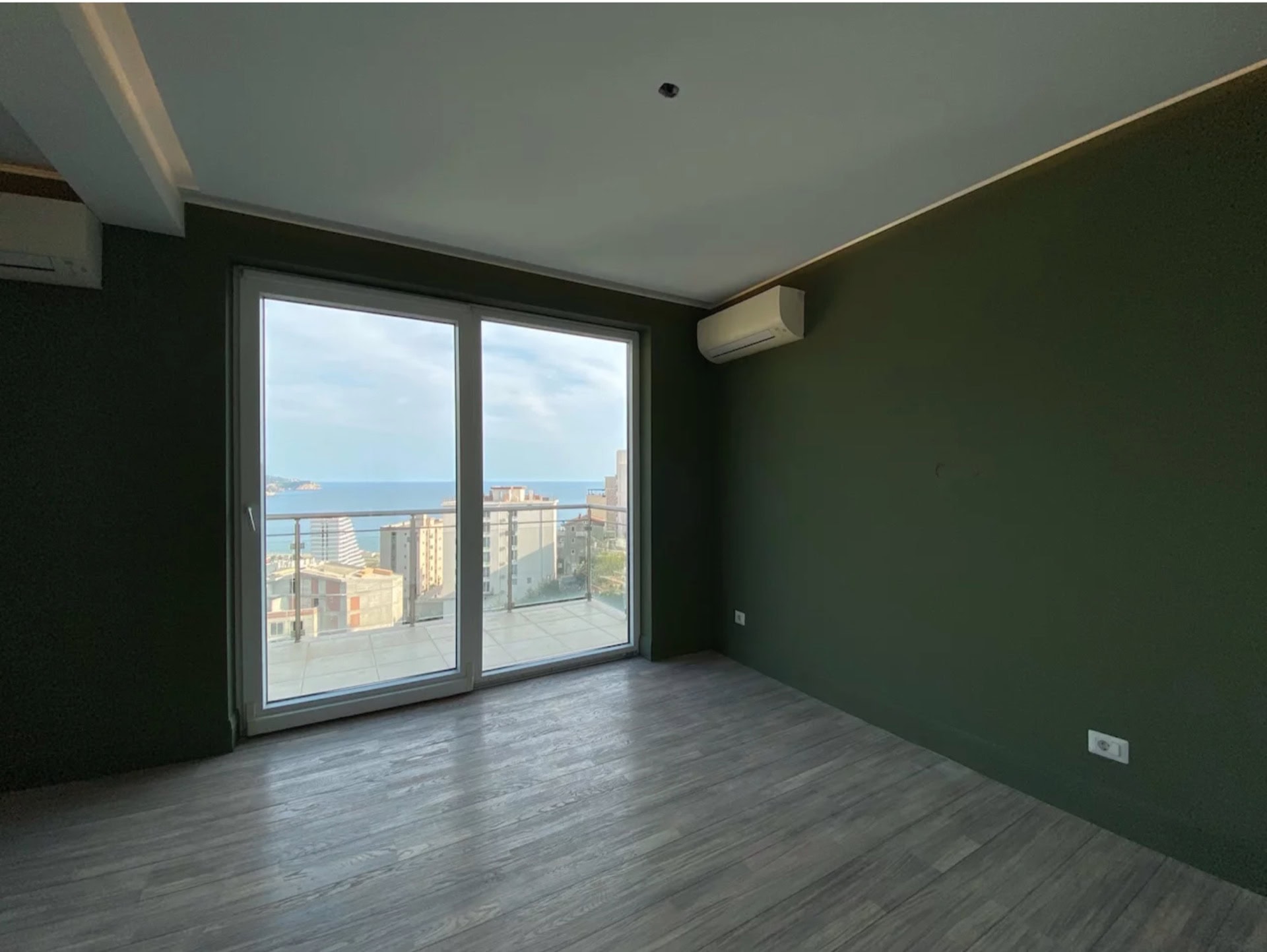 Wohnzimmer mit Panoramablick auf das Meer in einer Wohnung in Bečići, Montenegro: grüne Wände, heller Laminatboden und Terrasse.