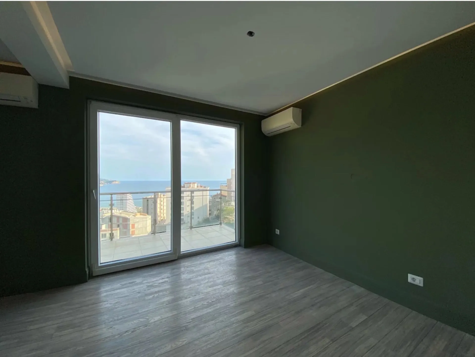 Living room with panoramic sea view in an apartment in Bečići, Montenegro: green walls, light laminate flooring, and a terrace.