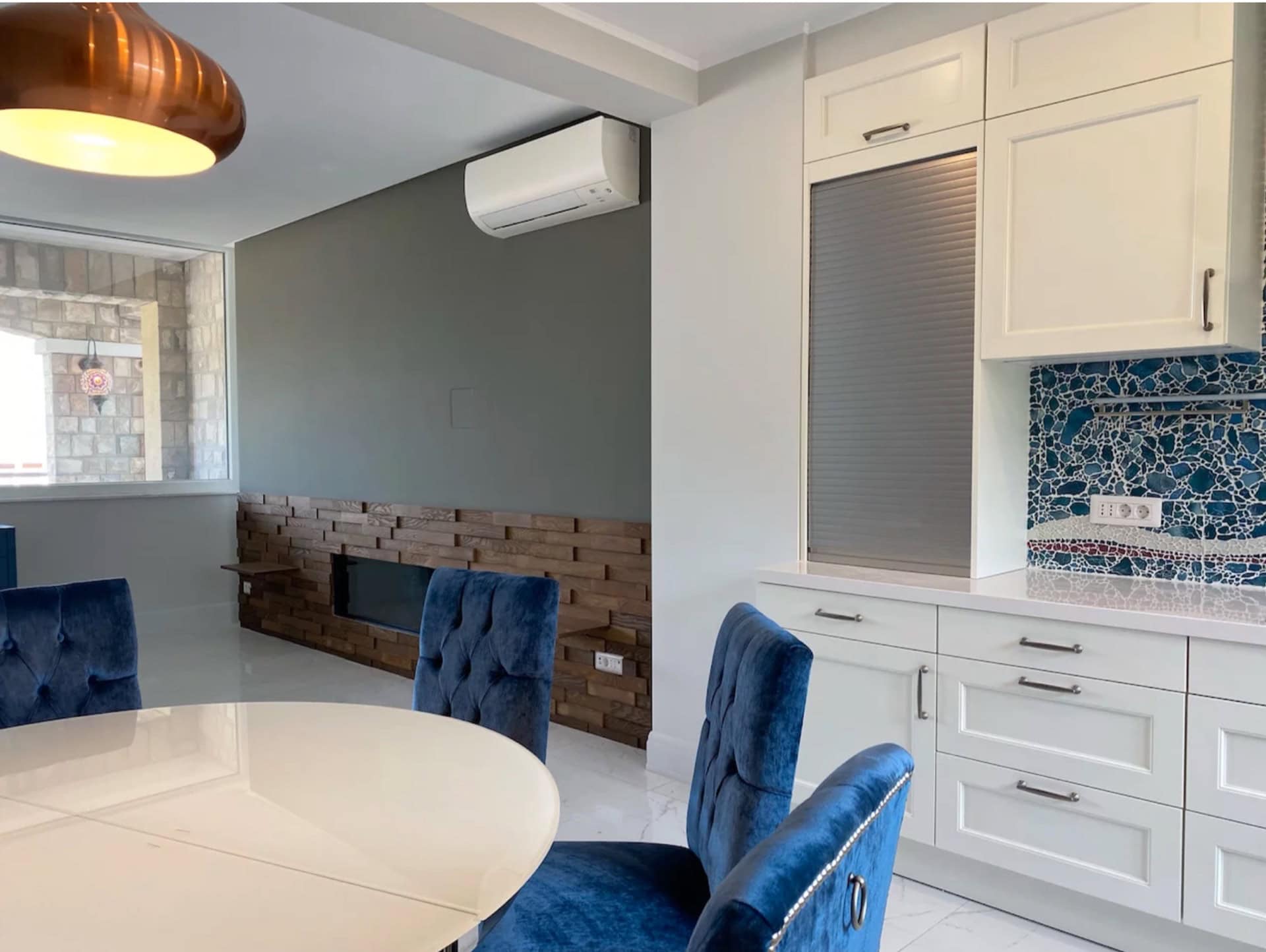 Moderne Küche in einer Wohnung in Bečići, Montenegro: weiße Fronten, blaue Samtstühle und Holzverkleidung.