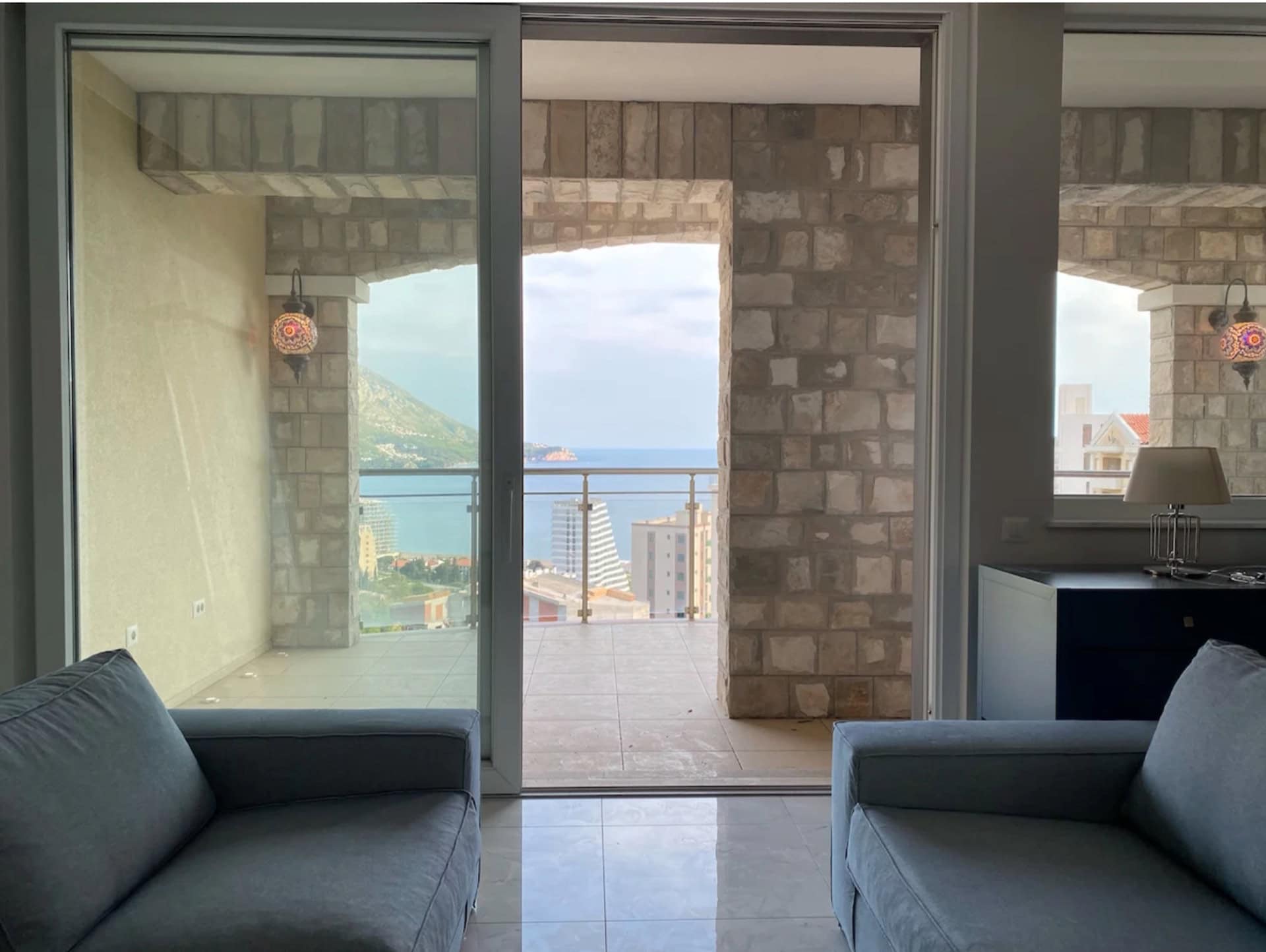 Wohnzimmer mit Panoramablick auf das Meer und die Berge in einer Wohnung, Bečići, Montenegro: Terrasse mit Steinverkleidung und Sofas.