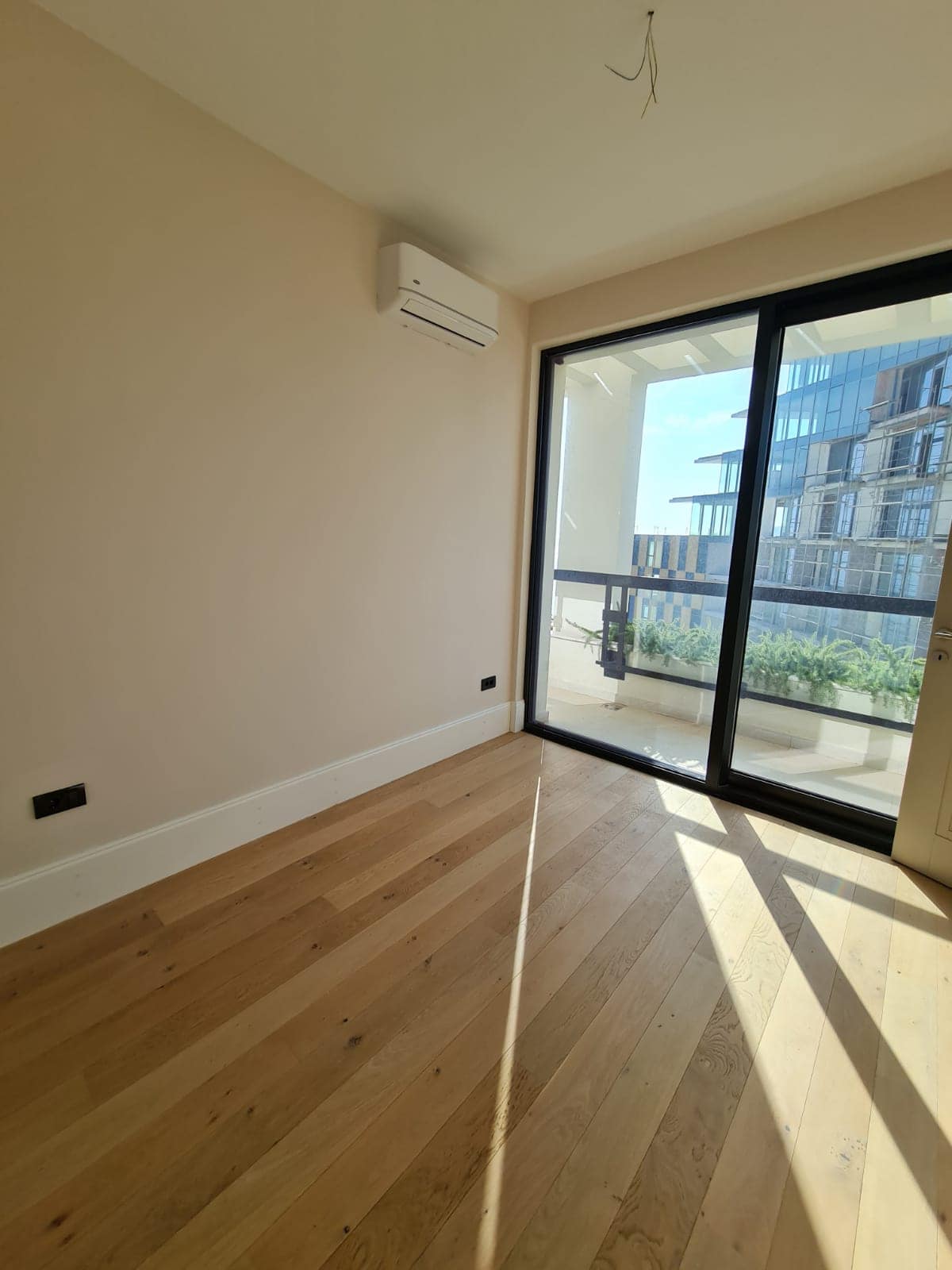 Chambre lumineuse avec parquet, climatisation et baie vitrée panoramique donnant sur la terrasse dans un appartement, Rafailovici, Monténégro.