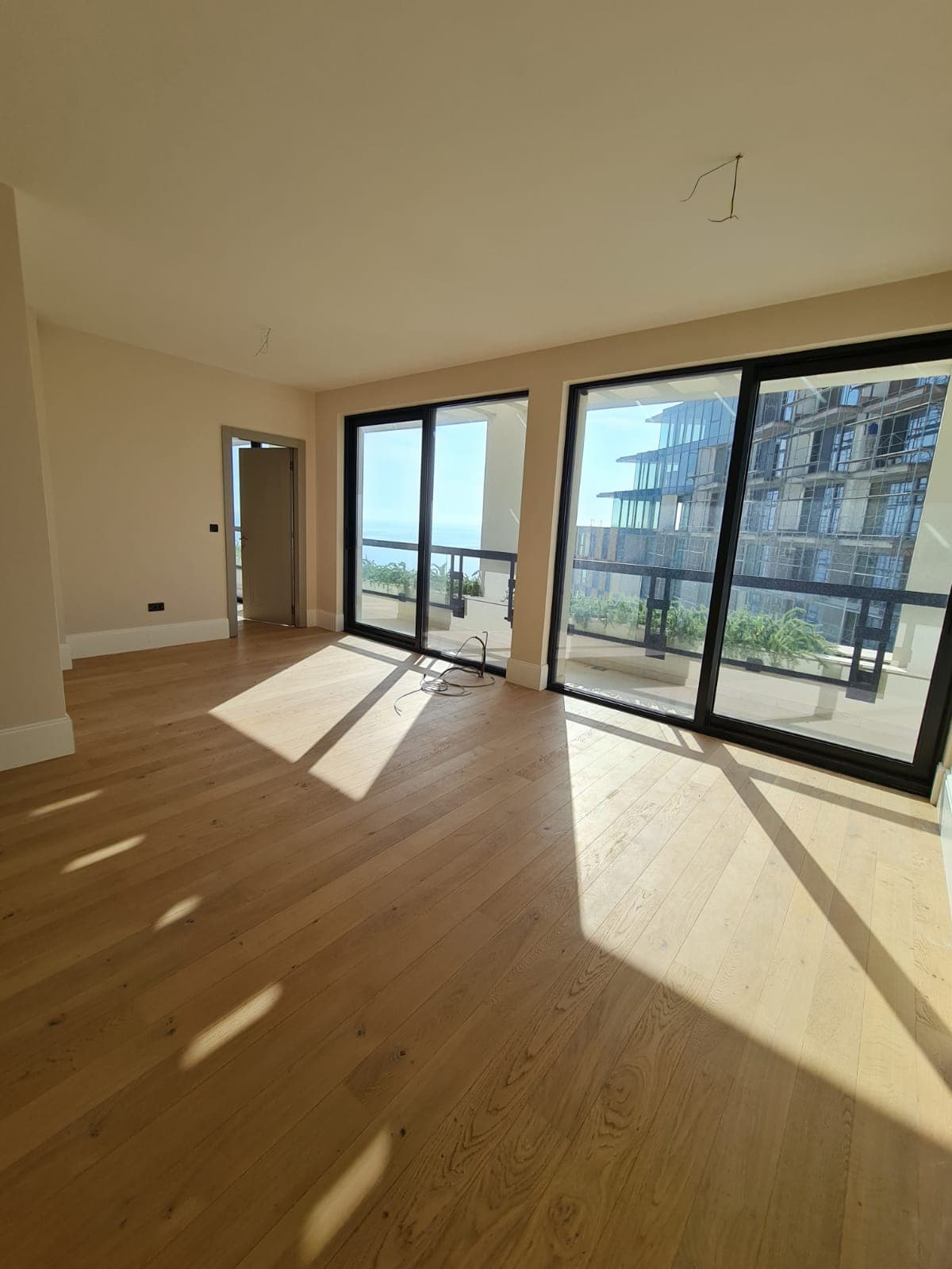 Salon lumineux dans un immeuble neuf à Rafailovići, Monténégro : baies panoramiques, vue sur la mer et parquet sans mobilier.
