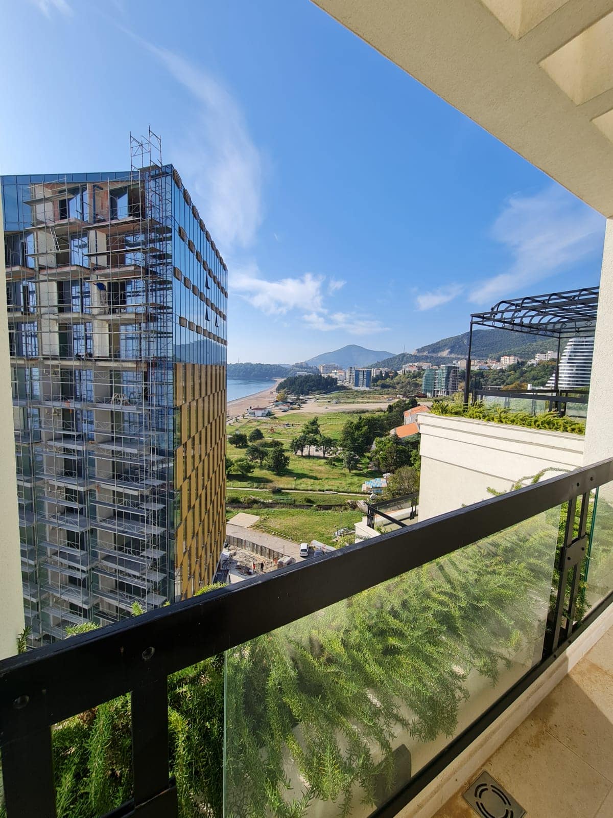 Vue depuis le balcon de l’appartement à Rafailovici, Monténégro : panorama sur la mer, les montagnes et un complexe résidentiel en construction à proximité.