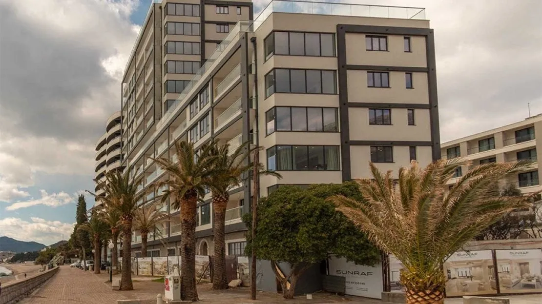 Modern multi-story residential complex with panoramic windows and palm trees along the waterfront in Bečići, Montenegro