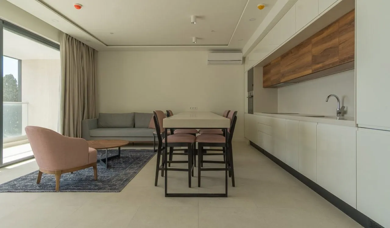 Modern kitchen-living room with furniture, panoramic window, and dining area in an apartment in Bečići, Montenegro.