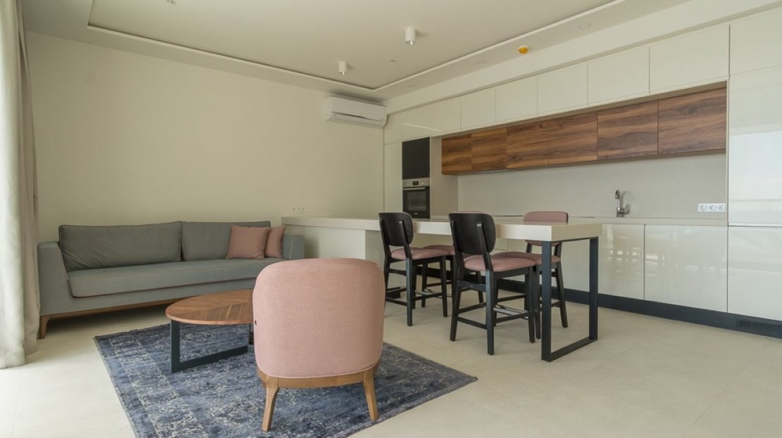 Modernes Wohnzimmer mit Küche, grauem Sofa, rosa Sessel und Essbereich in einer Wohnung in Bečići, Montenegro