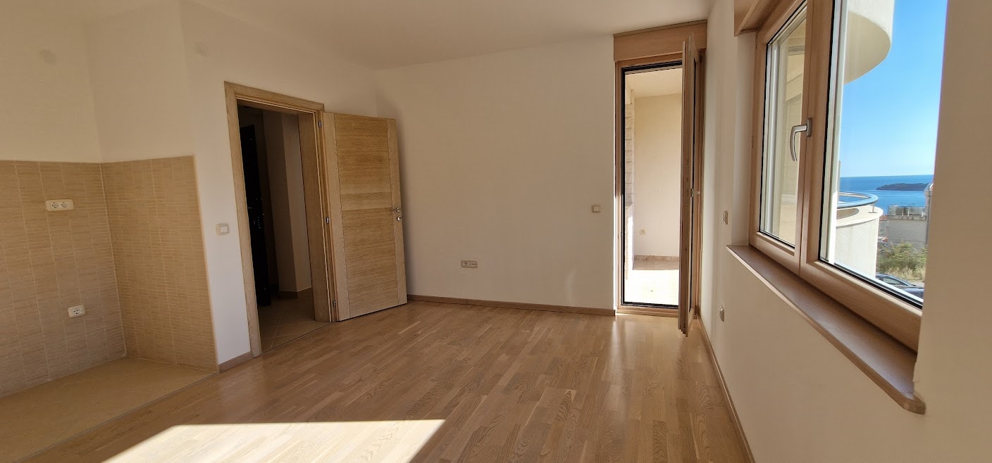 Helles Wohnzimmer mit Parkett und Zugang zum Balkon in einer Wohnung in Bečići, Montenegro, mit Panoramablick auf das Meer.