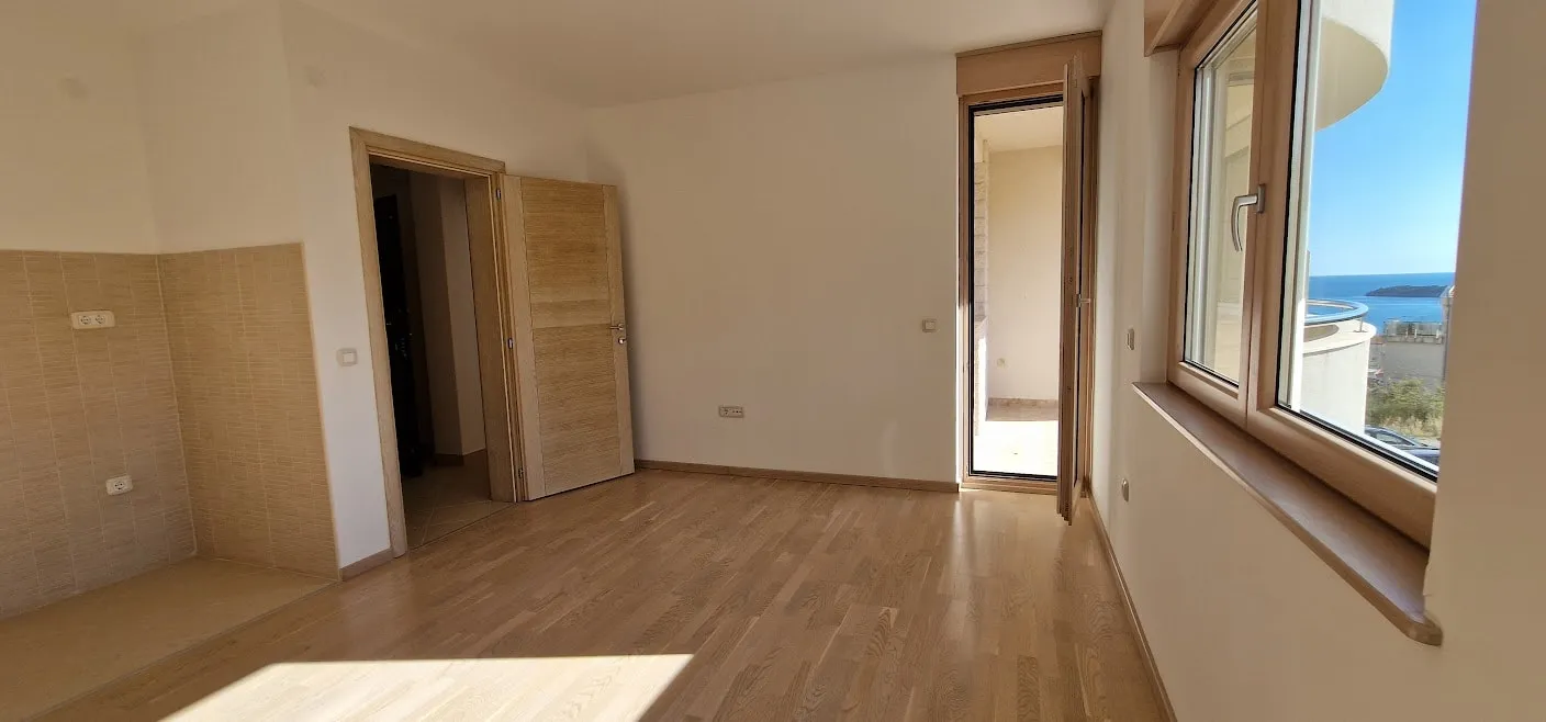 Bright living room with parquet flooring and access to the balcony in an apartment in Bečići, Montenegro, with panoramic sea views.