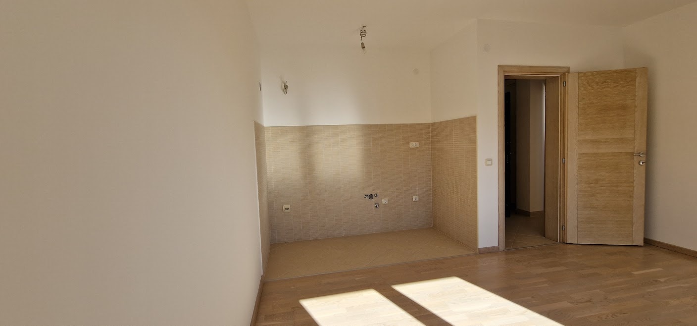 Küchenbereich in einer Wohnung in Bečići, Montenegro: helle Ausstattung, Fliesenspiegel, Parkettboden und Innentür.