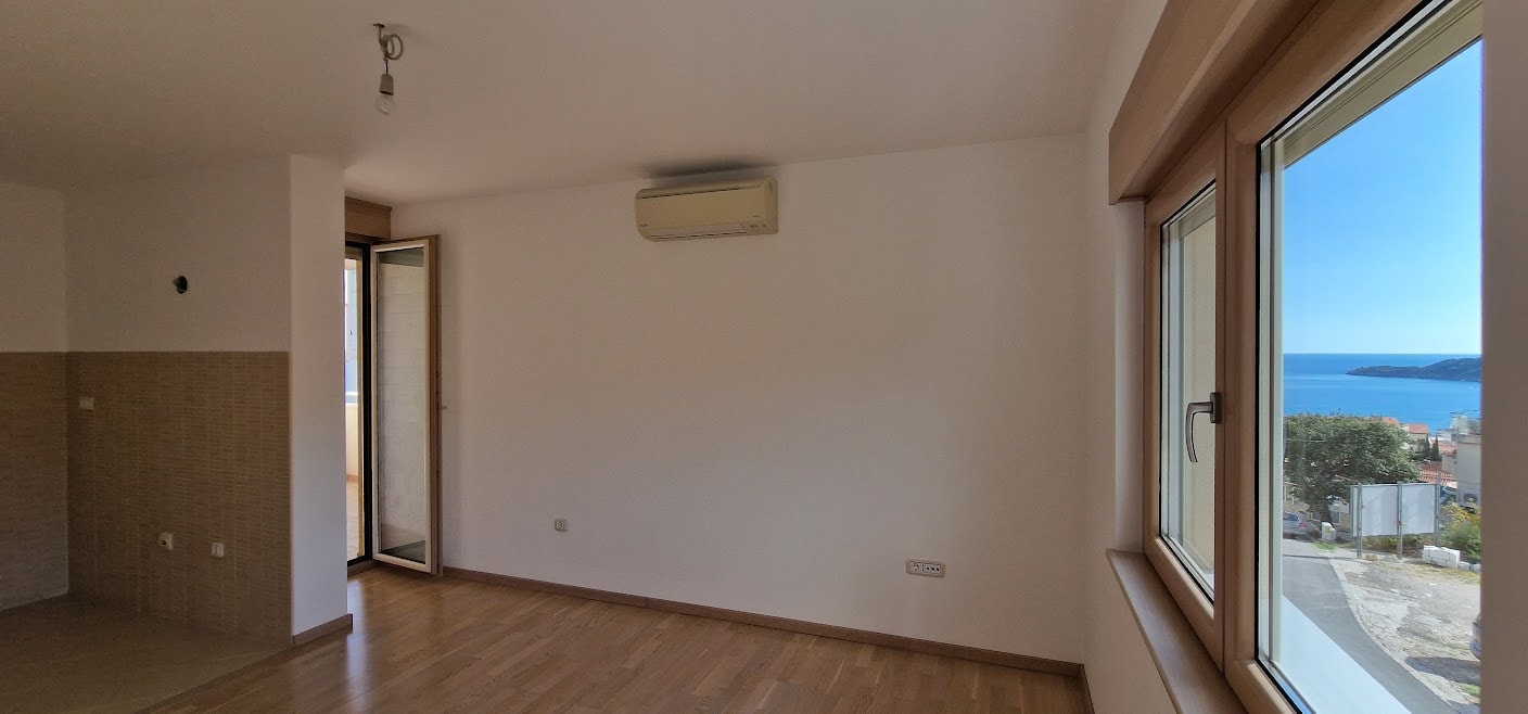 Helles Wohnzimmer in einer Wohnung in Bečići, Montenegro: Parkettboden, Klimaanlage und Panoramablick auf das Meer aus dem Fenster.