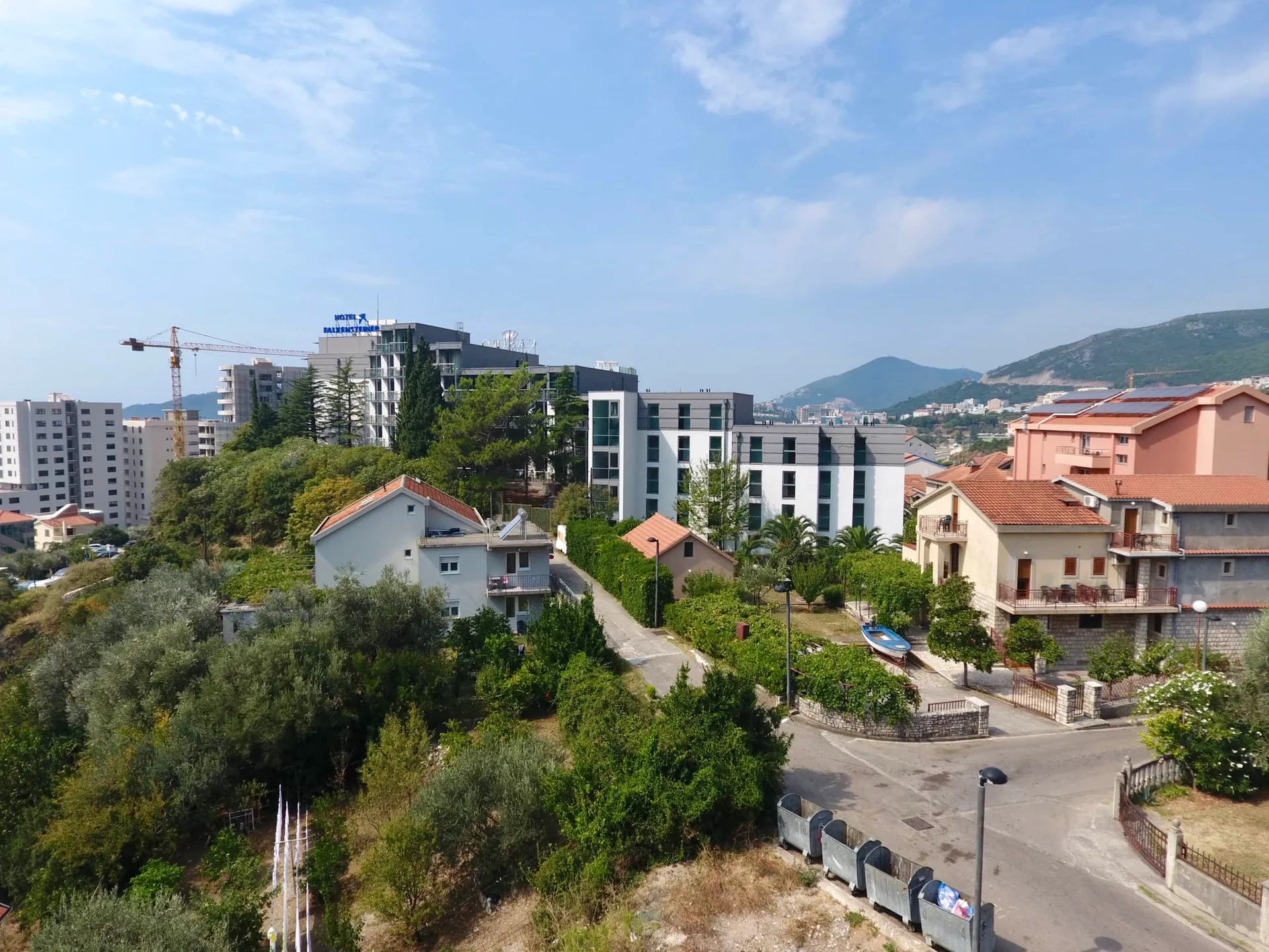 Erhöhte Ansicht einer Küstenstadt mit modernen Hotels, traditionellen Häusern und viel Grün.