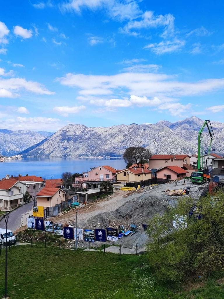 Plac budowy kompleksu mieszkaniowego w Dobrocie, Czarnogóra, z panoramicznym widokiem na Zatokę Kotorską i góry.