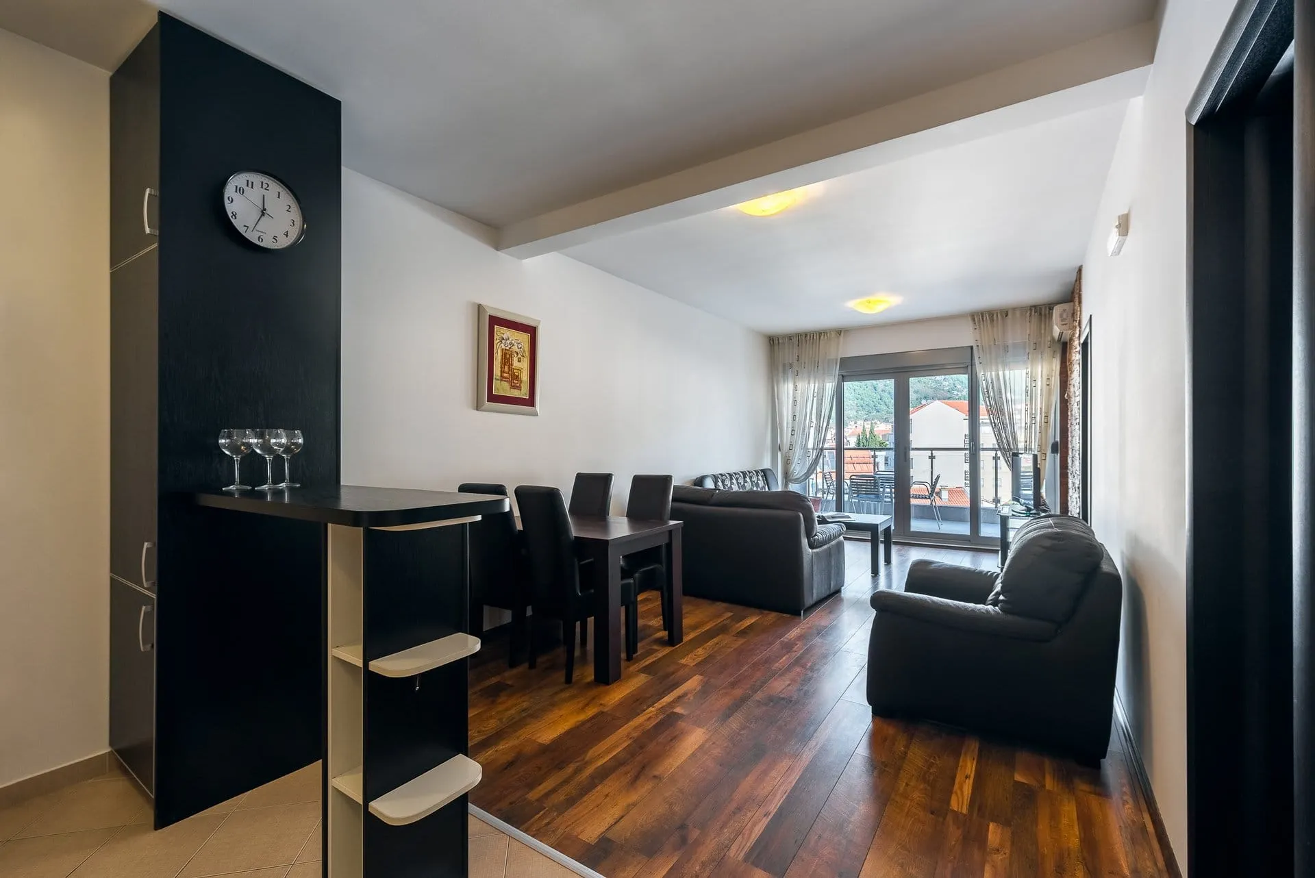 Salon z ciemnymi meblami, jadalnią i wyjściem na balkon w mieszkaniu w Budvie, Czarnogóra.