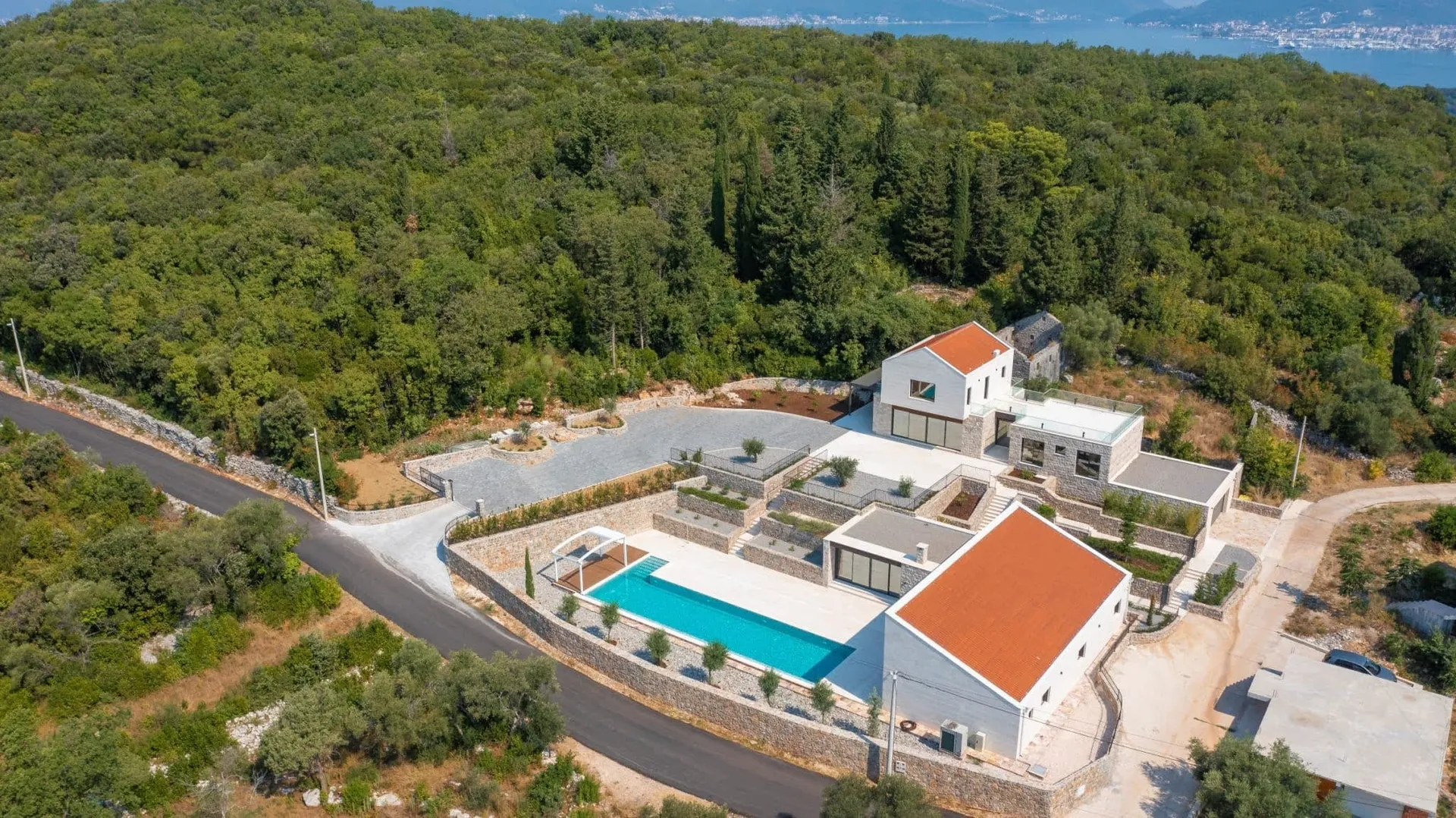 Luftaufnahme einer großen modernen Villa mit Swimmingpool und rotem Ziegeldach, umgeben von einem grünen Wald.