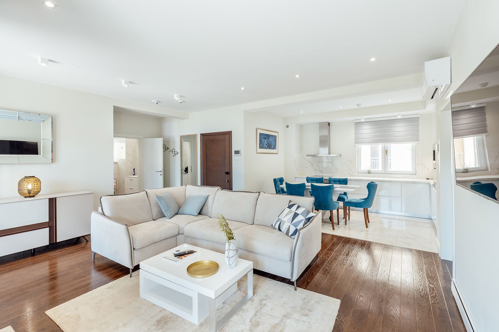Modernes Wohnzimmer mit beigem Sofa und Küche in einer Wohnanlage in Kumbor, Montenegro: stilvolles Interieur, Parkett und helle Möbel.
