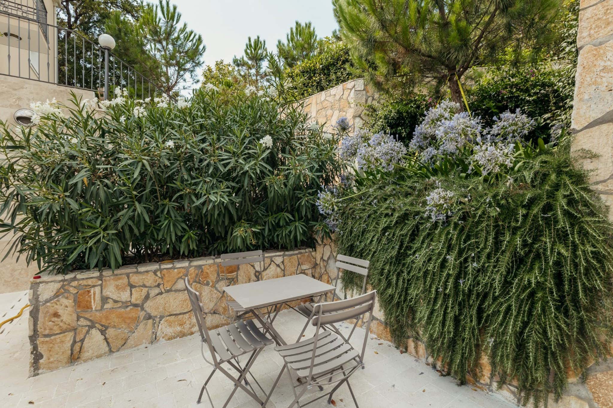 Gemütliche Terrasse mit Gartenmöbeln in einer Wohnanlage in Kumbor, Montenegro, umgeben von einem blühenden Garten und Steinmauern.