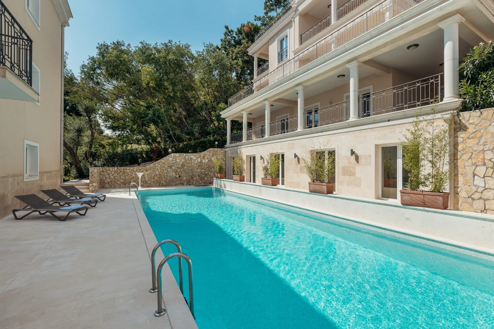 Offener Pool mit Liegestühlen an einer exklusiven Wohnanlage in Kumbor, Montenegro, mit Steinverkleidung und Terrasse.