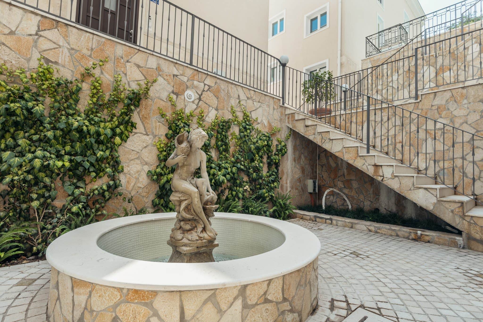 Brunnen mit Statue und Steintreppe im Innenhof einer Wohnanlage in Kumbor, Montenegro.