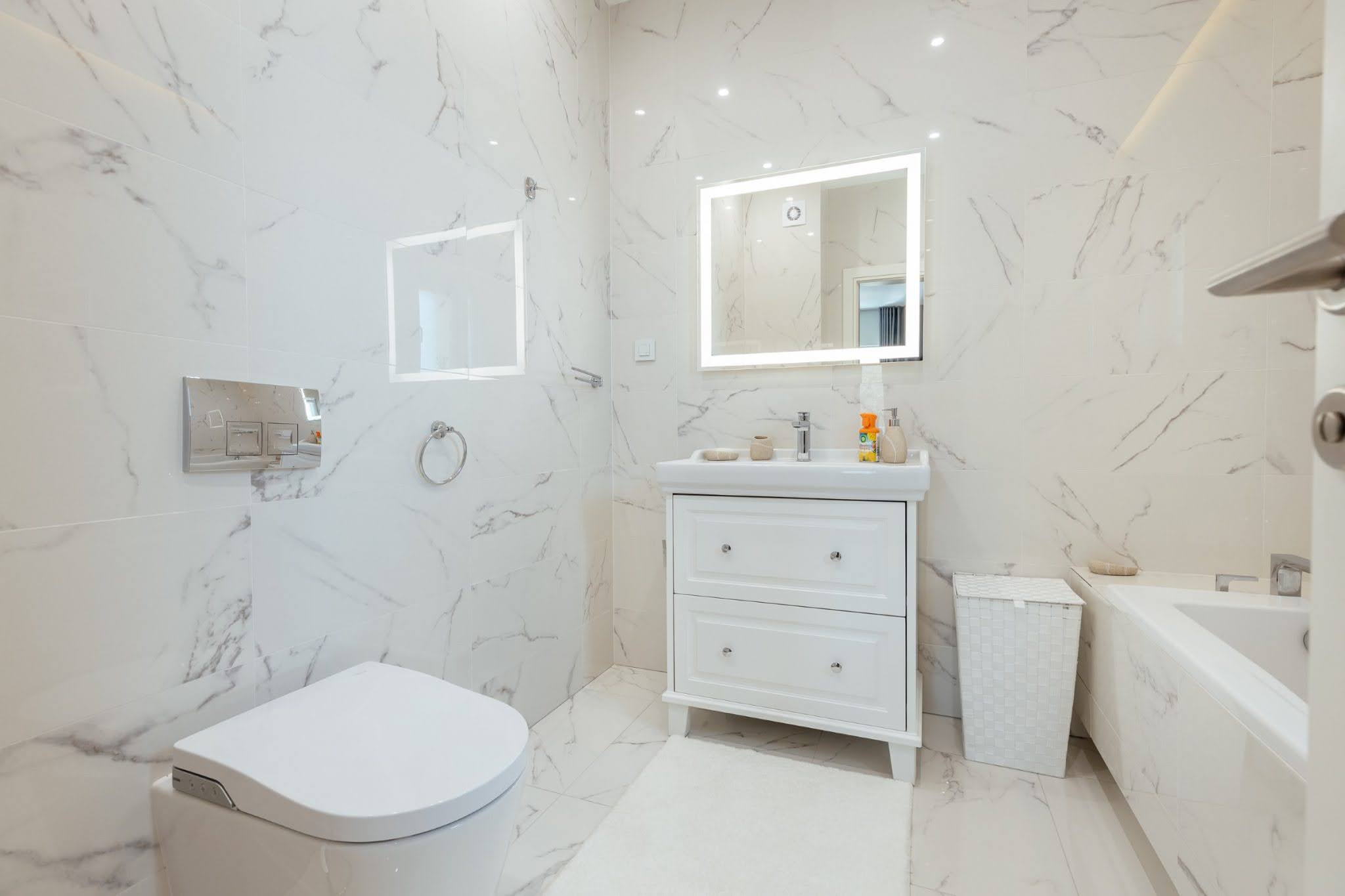 Modernes Badezimmer mit weißer Marmoroptik im ЖК Kumbor, Montenegro: Waschtisch, Spiegel mit Beleuchtung und Badewanne.