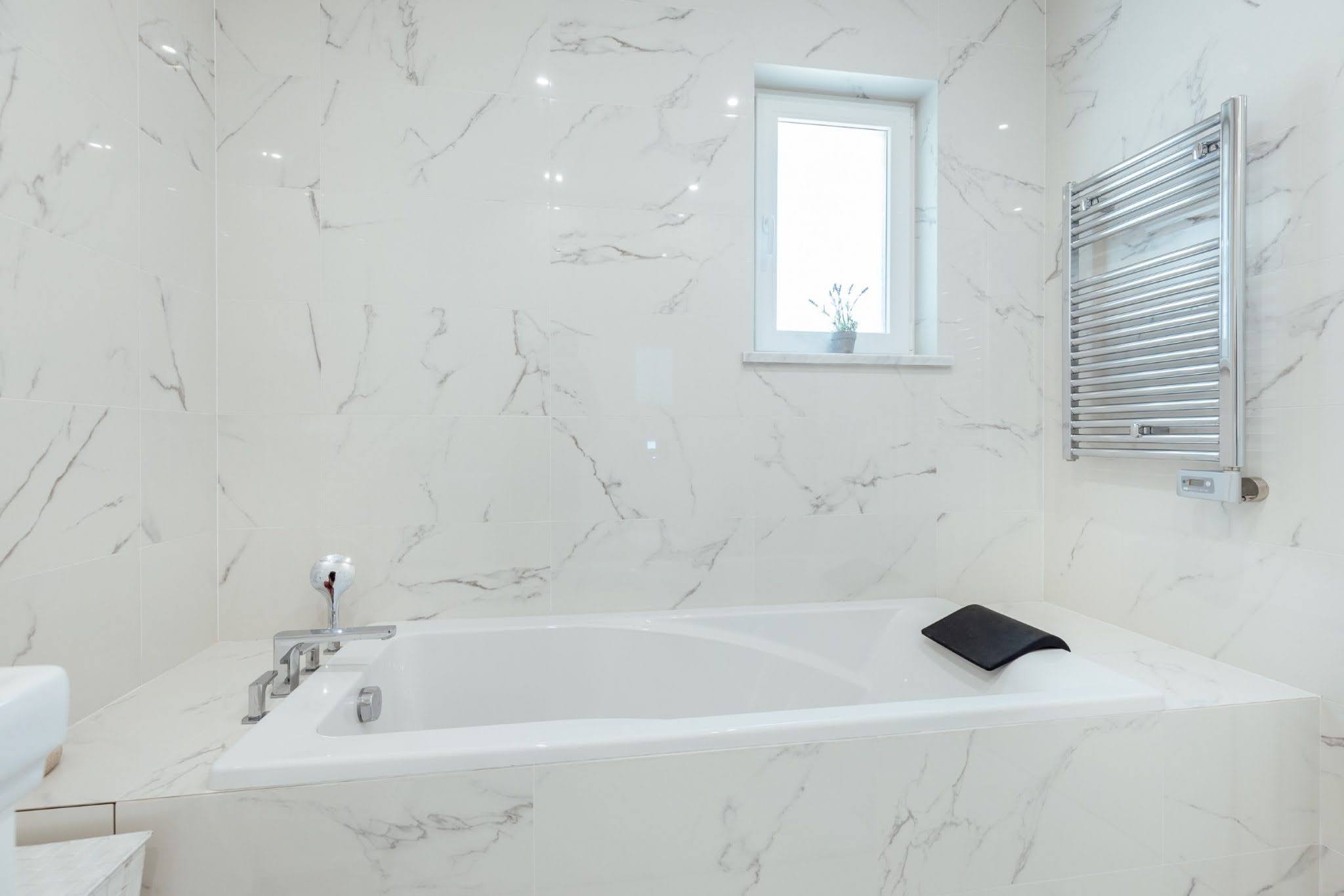 Modernes Badezimmer im ЖК Kumbor, Montenegro: weiße Marmoroptik-Fliesen, eingebaute Badewanne und Handtuchheizkörper.