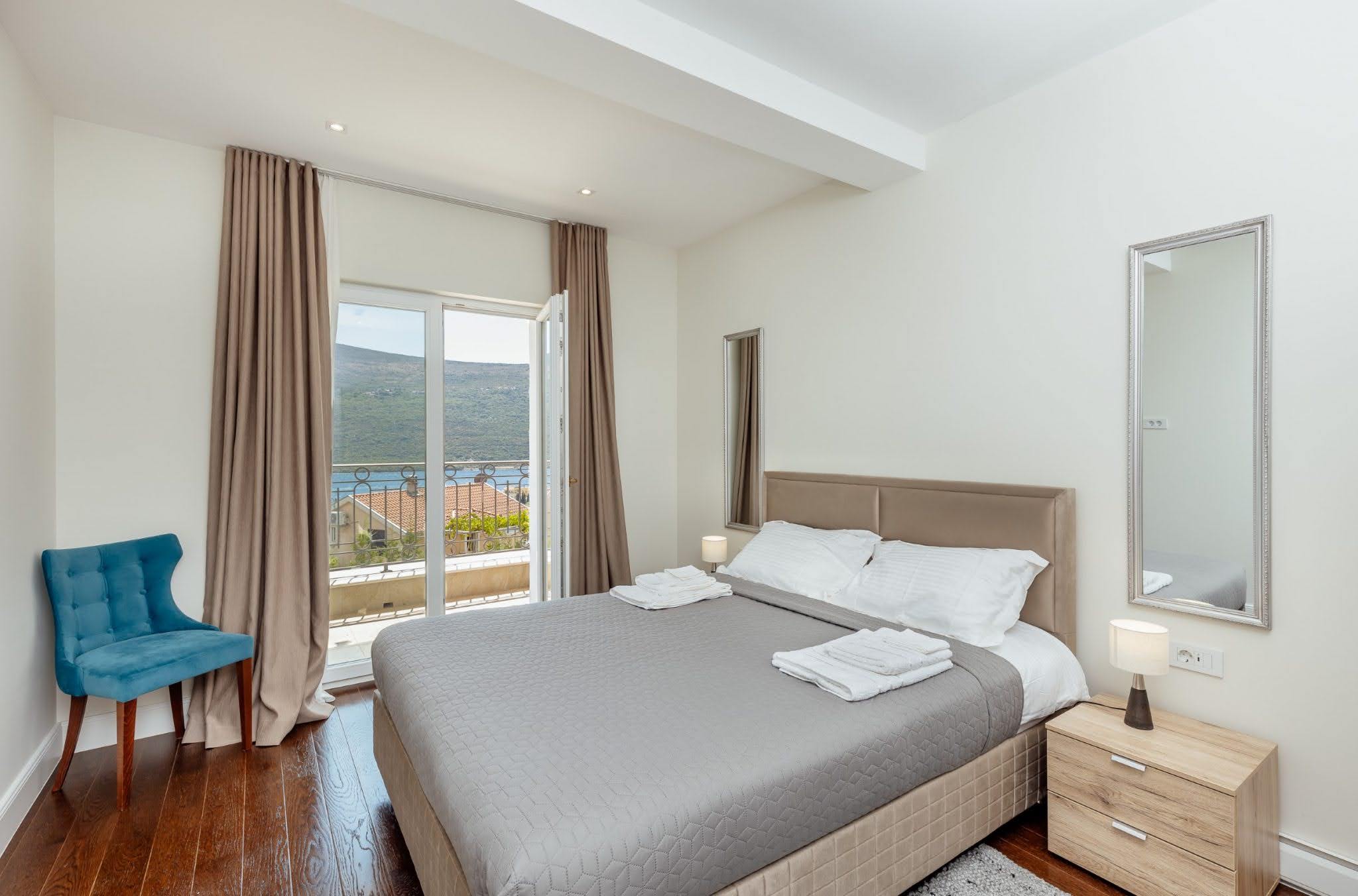 Schlafzimmer in der Wohnanlage Kumbor, Montenegro: Doppelbett, blauer Sessel und Zugang zum Balkon mit Meer- und Bergblick.