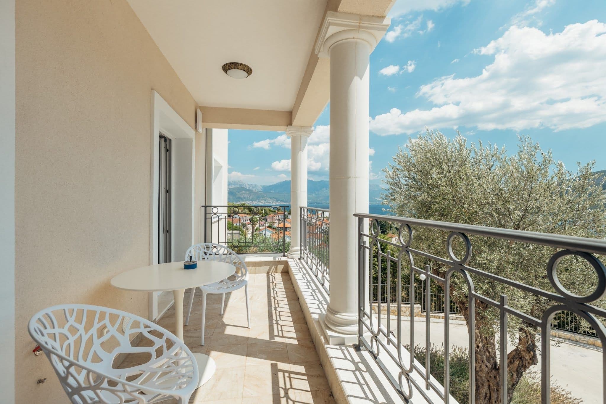 Balkon mit Säulen und Meerblick in einer Wohnanlage in Kumbor, Montenegro: weiße Möbel und schmiedeeisernes Geländer.