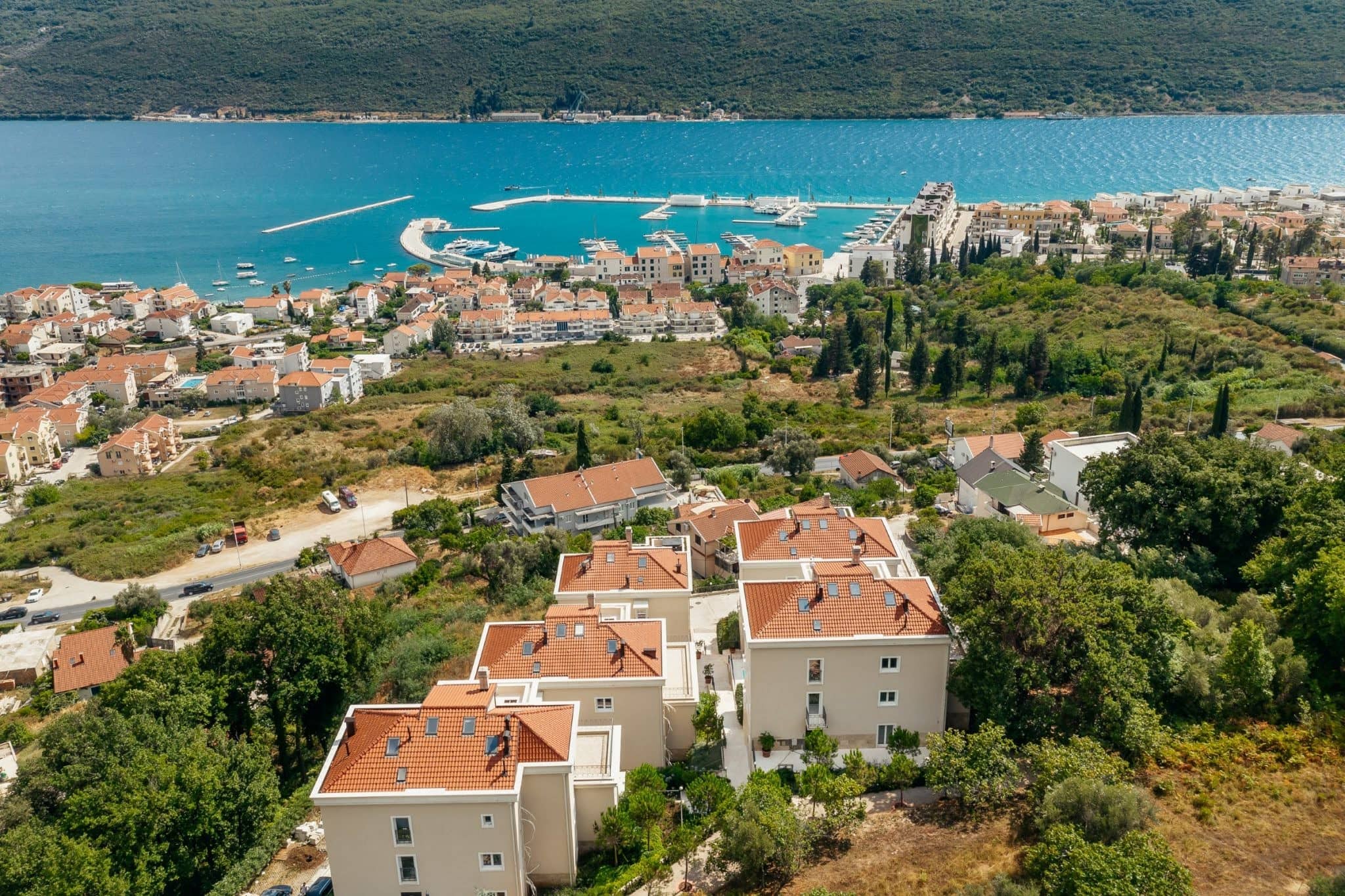 Luftaufnahme einer Wohnanlage in Kumbor, Montenegro: moderne Häuser mit Ziegeldächern und Panoramablick auf das Meer.