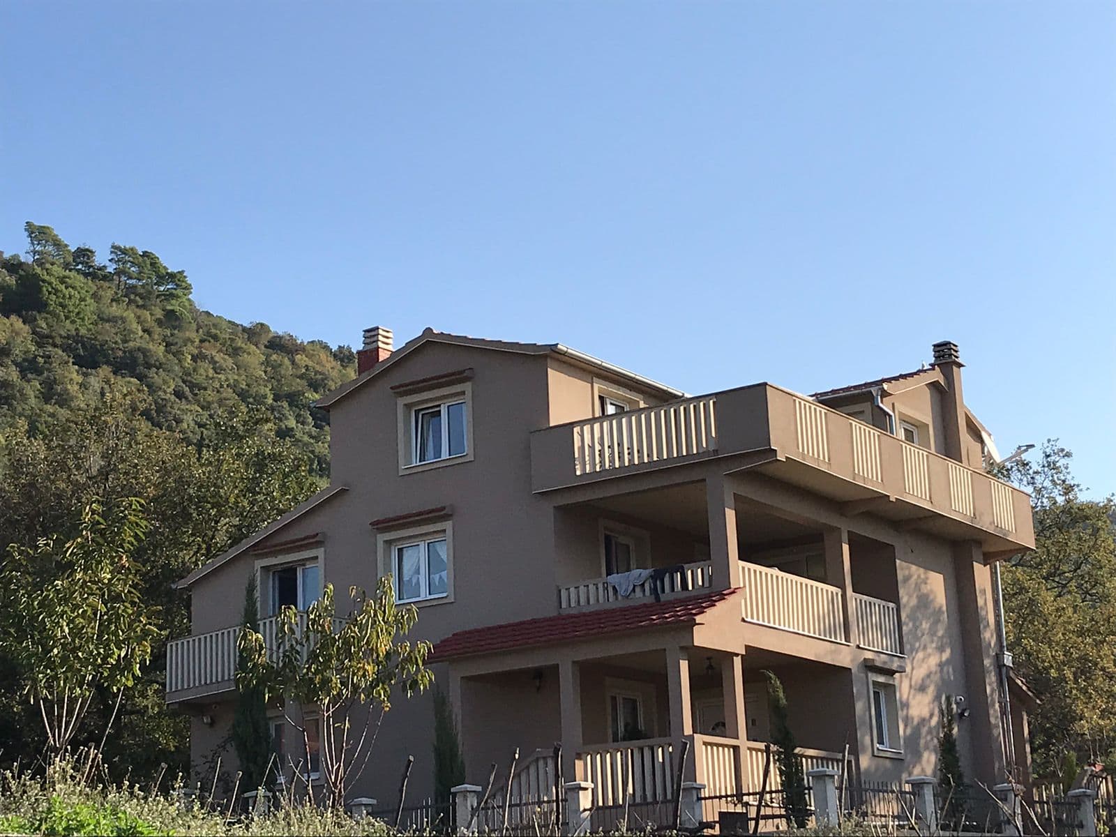 Dreistöckiges Einfamilienhaus mit Terrassen und Bergblick in Luštica, Montenegro. Hausfassade umgeben von Grün.