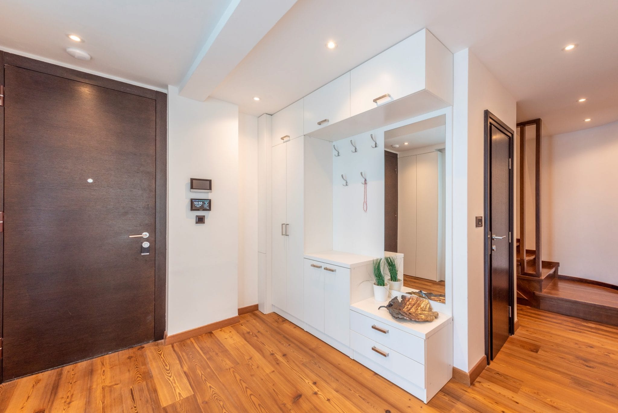 Moderne Diele in einem Penthouse in Bečići, Montenegro: weißer Schrank mit Spiegel, dunkle Türen und Parkettboden.