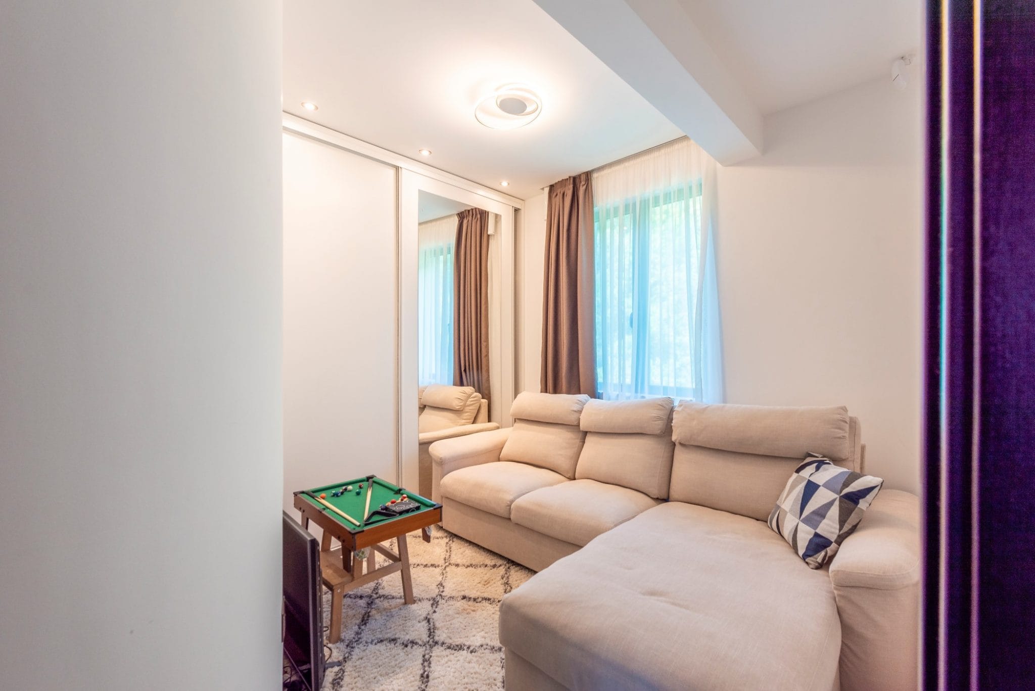 Helles Wohnzimmer mit beigem Sofa und Spiegelschrank im Penthouse, Bečići, Montenegro. Innenraum mit Teppich und Mini-Billard.