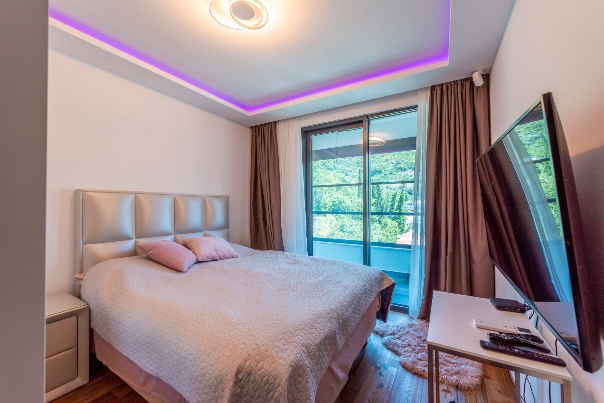 Modernes Schlafzimmer im Penthouse in Bečići, Montenegro: Doppelbett, Panoramafenster mit Bergblick und LED-Beleuchtung.