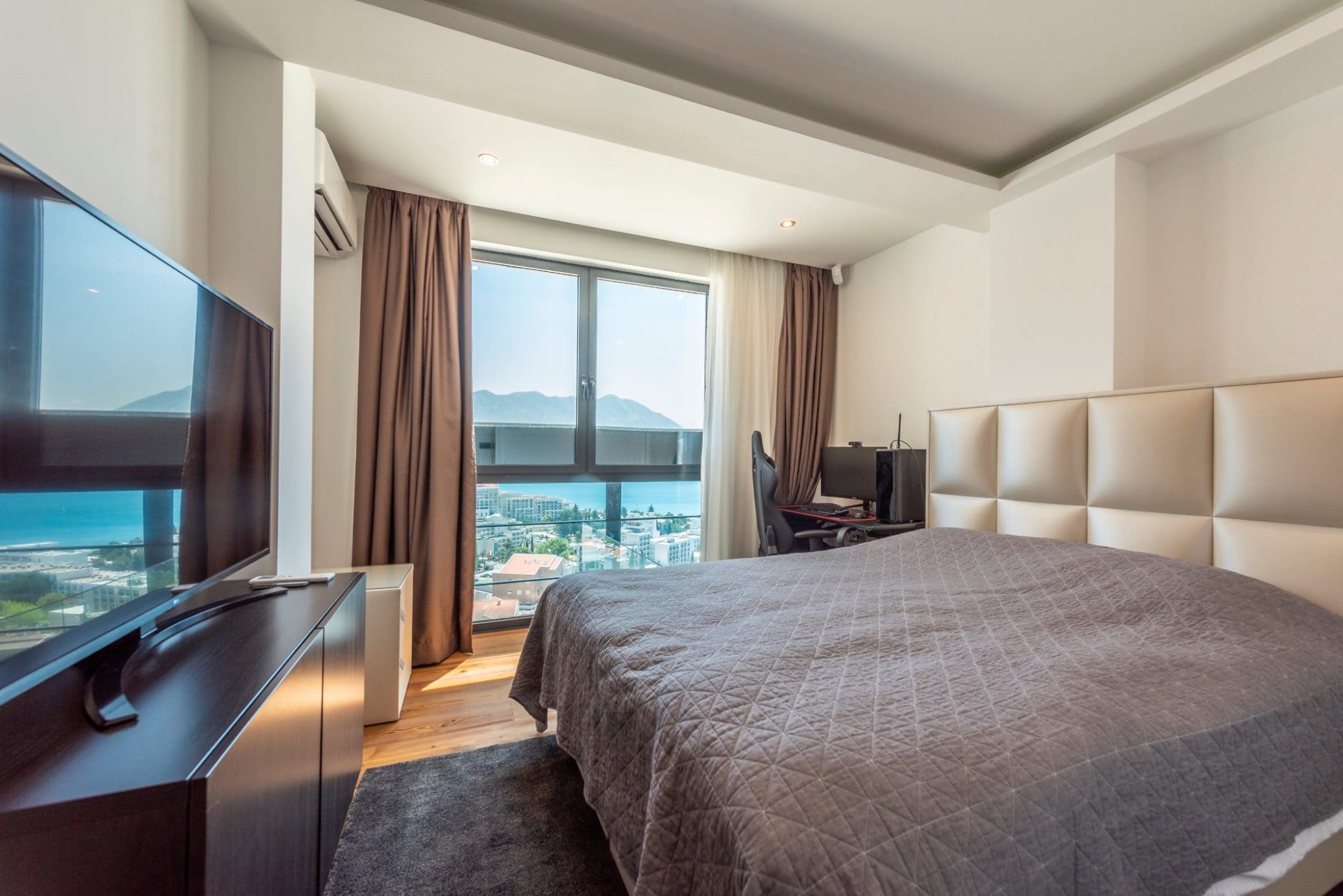 Schlafzimmer im Penthouse in Bečići, Montenegro: Doppelbett, Arbeitsbereich und Panoramablick auf das Meer und die Berge.